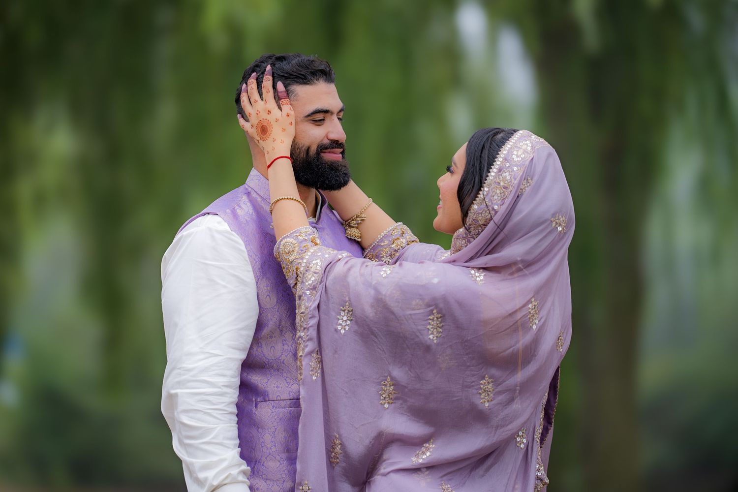 A tender moment between a couple wearing coordinated purple and white traditional attire.