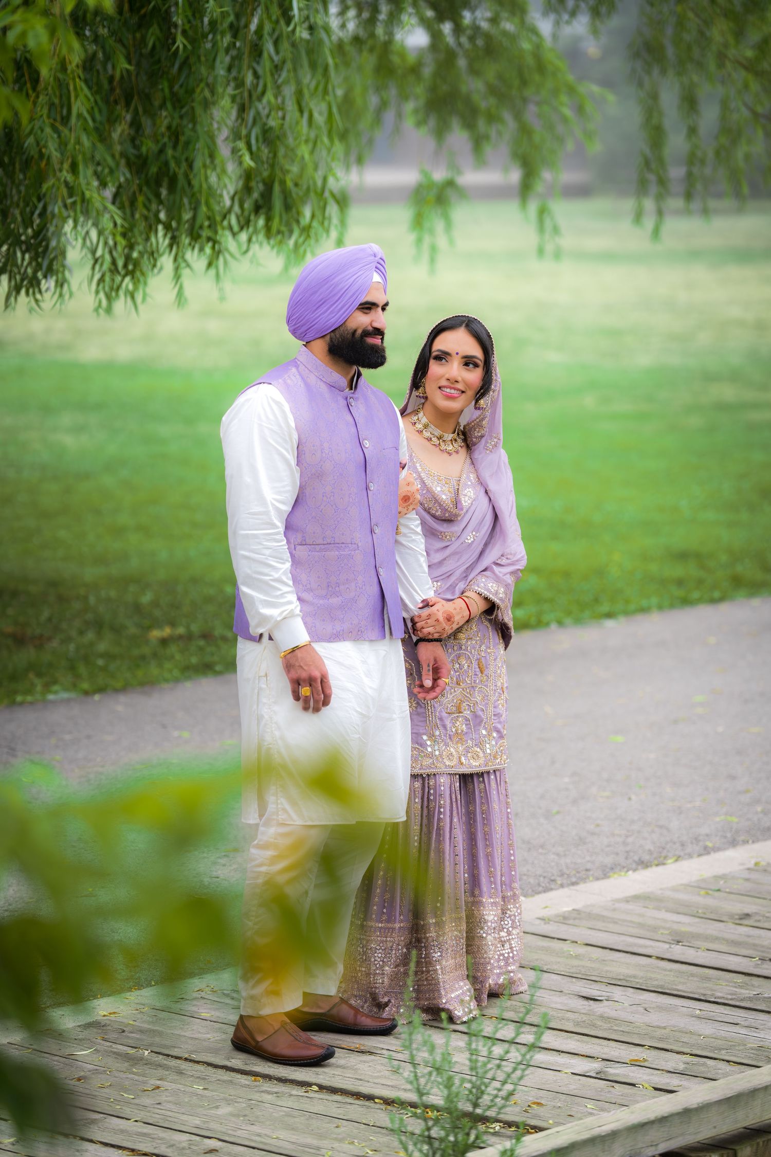 A couple in coordinated purple outfits standing on a wooden deck surrounded by greenery.