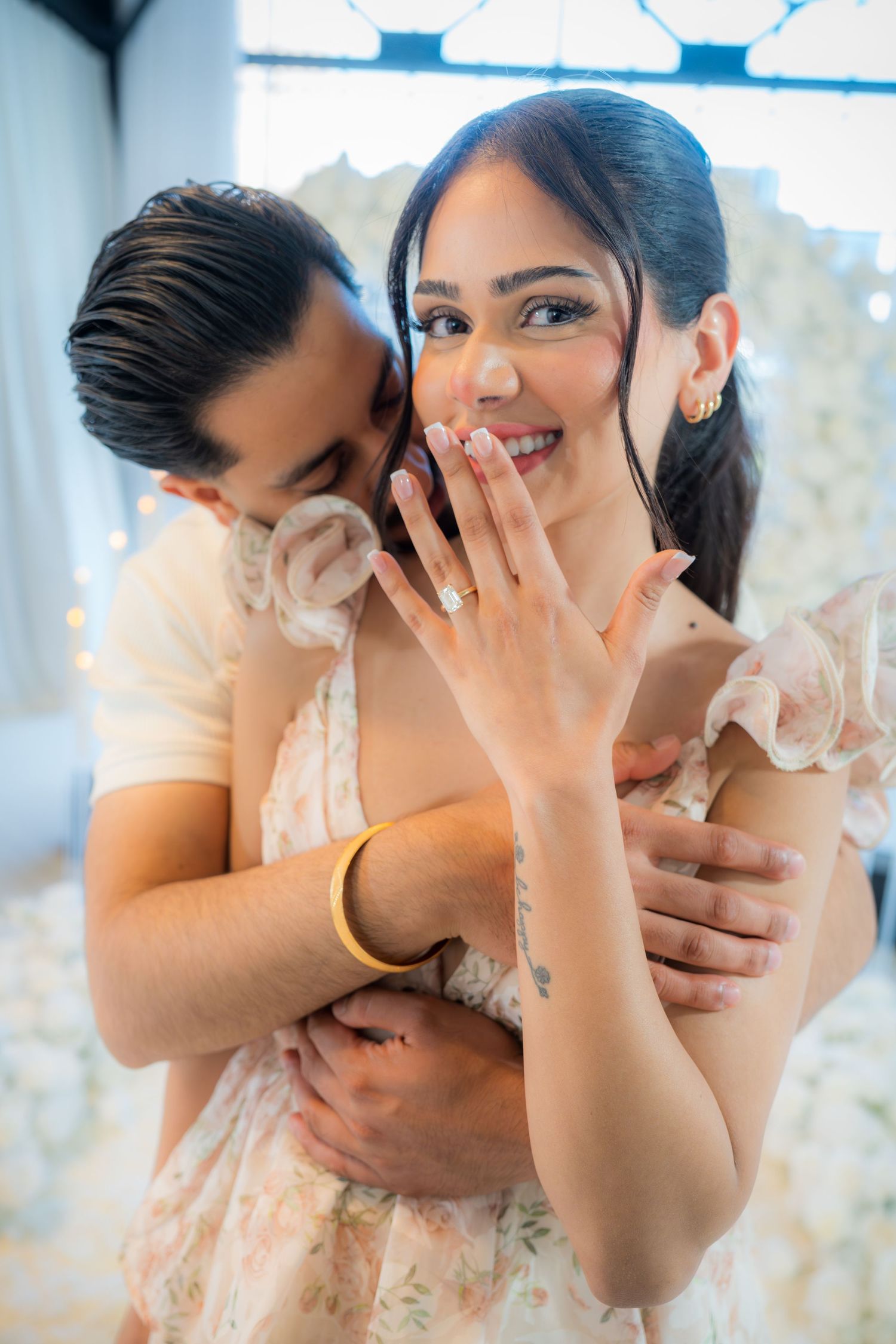 Joyful woman showing off her engagement ring while her partner embraces her from behind.