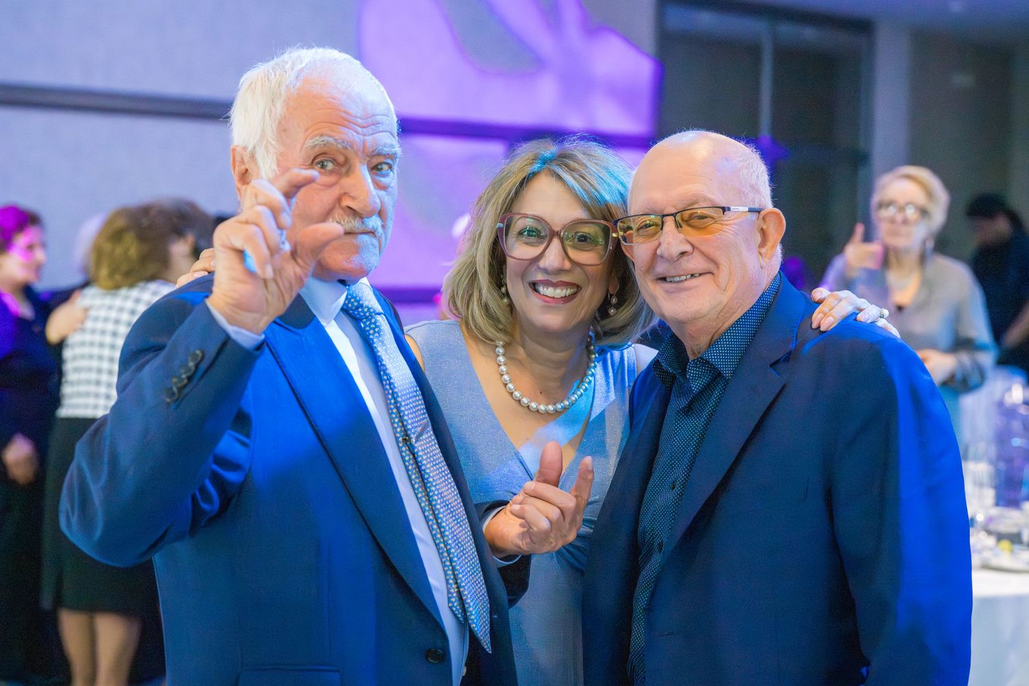 Three smiling adults pose together at a formal event, holding small awards in a banquet hall.