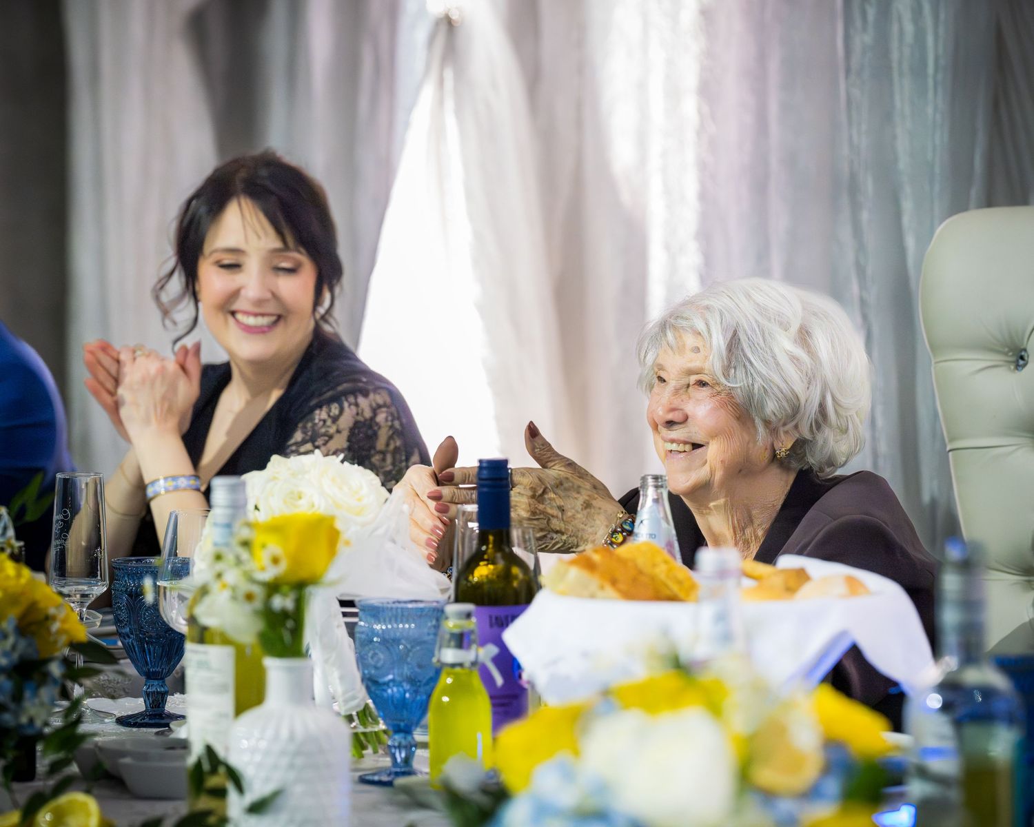 Two women laughing joyfully together at decorated wedding anniversary reception table.
