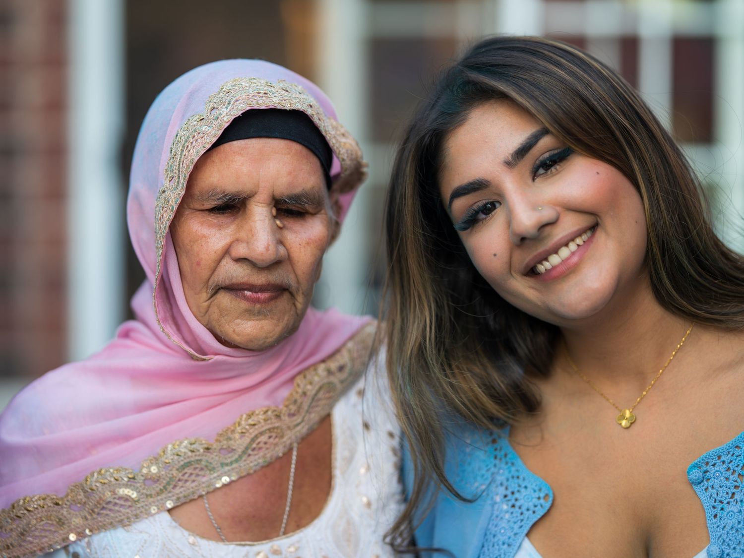 Elderly woman in pink hijab and young woman smiling together at an outdoor family celebration.