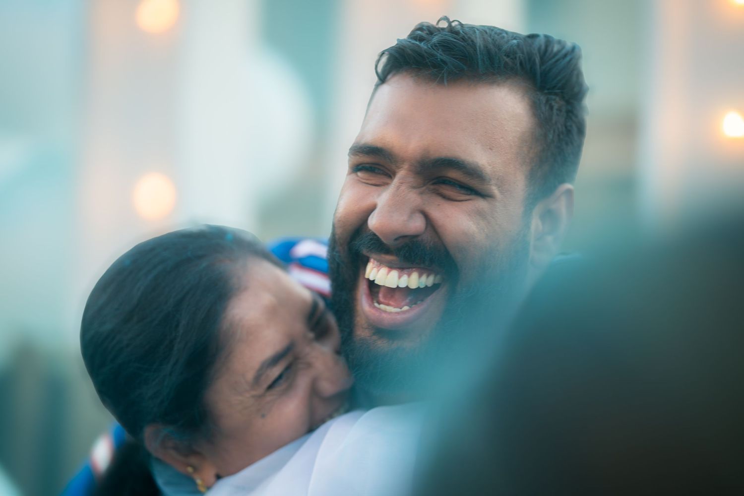 Joyful man laughs as a woman hugs him warmly at an outdoor celebration event.