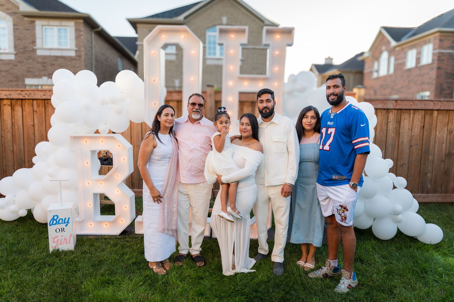 Family group photo at a gender reveal party with BOY balloon letter backdrop and white balloon arch in backyard.