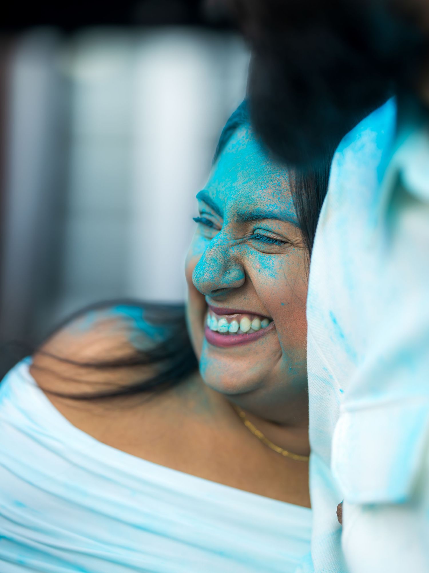 Woman laughing joyfully with blue gender reveal powder on her face at an outdoor celebration.