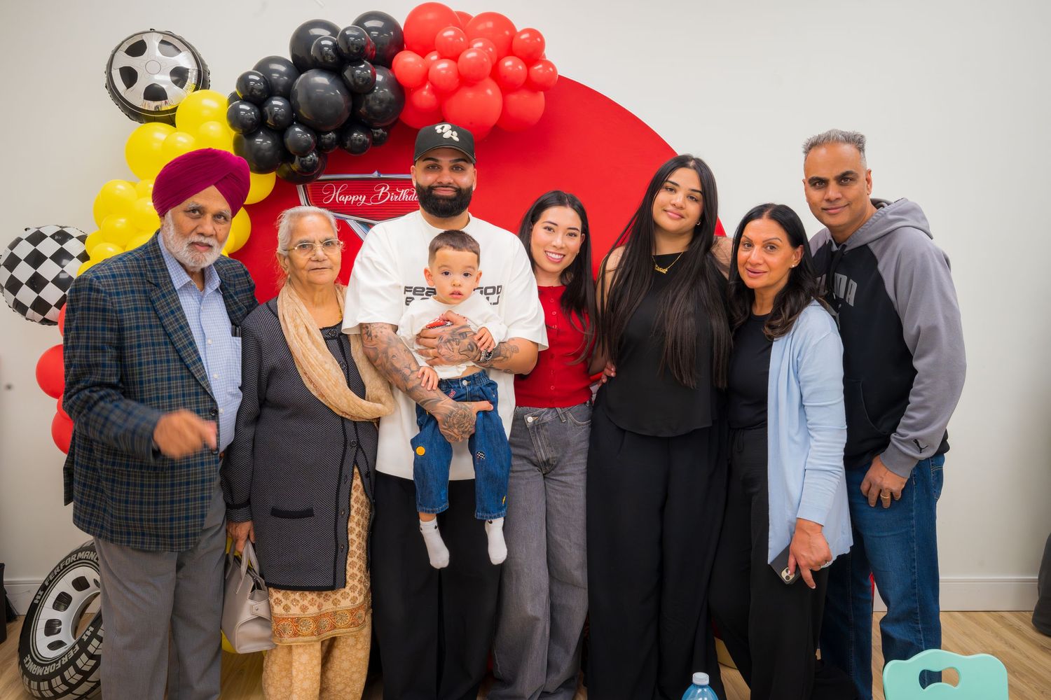 Family group of seven posing at a racing-themed birthday party with balloons.