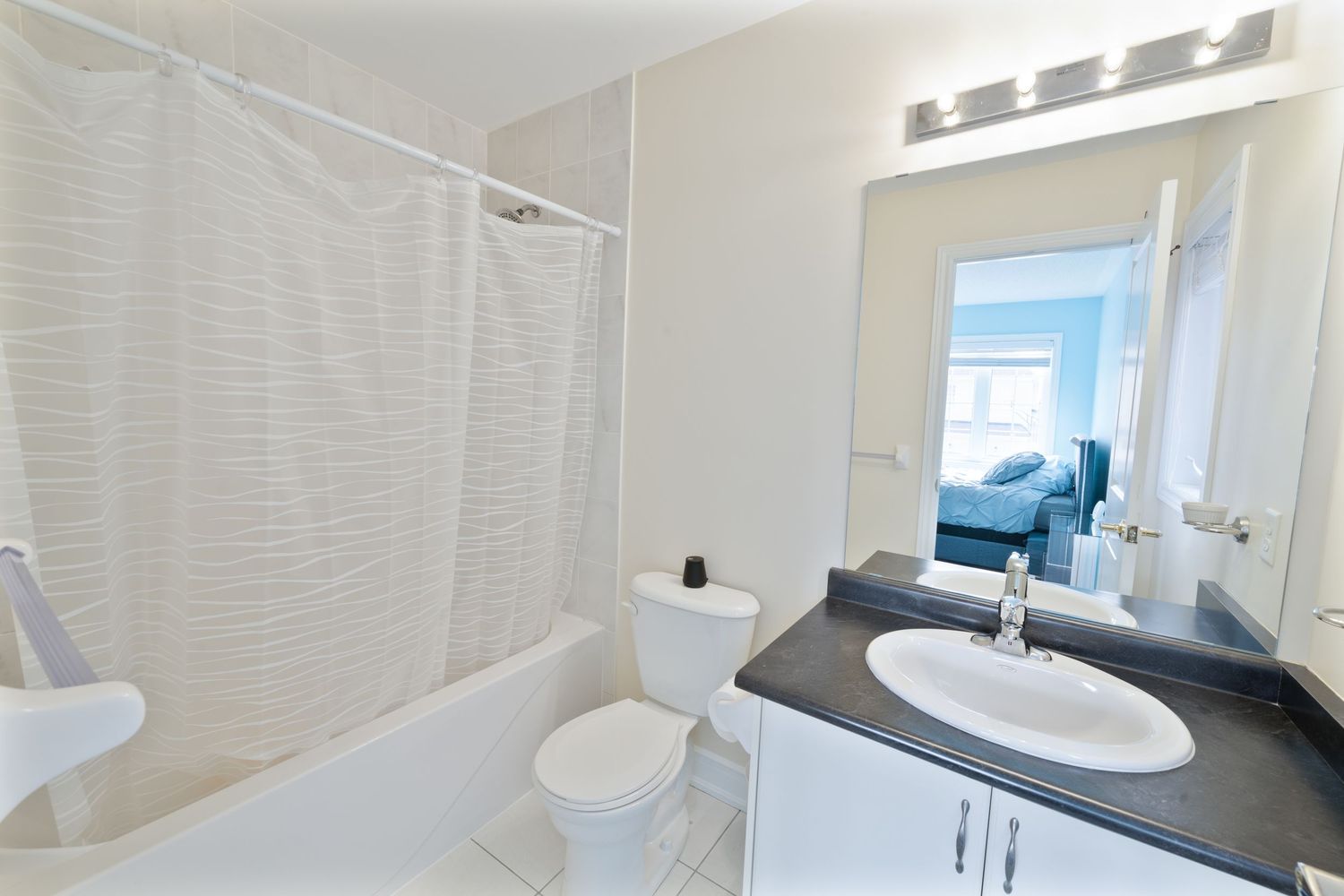 Modern white bathroom interior with black countertop vanity, oval sink, and shower curtain in bright natural lighting.