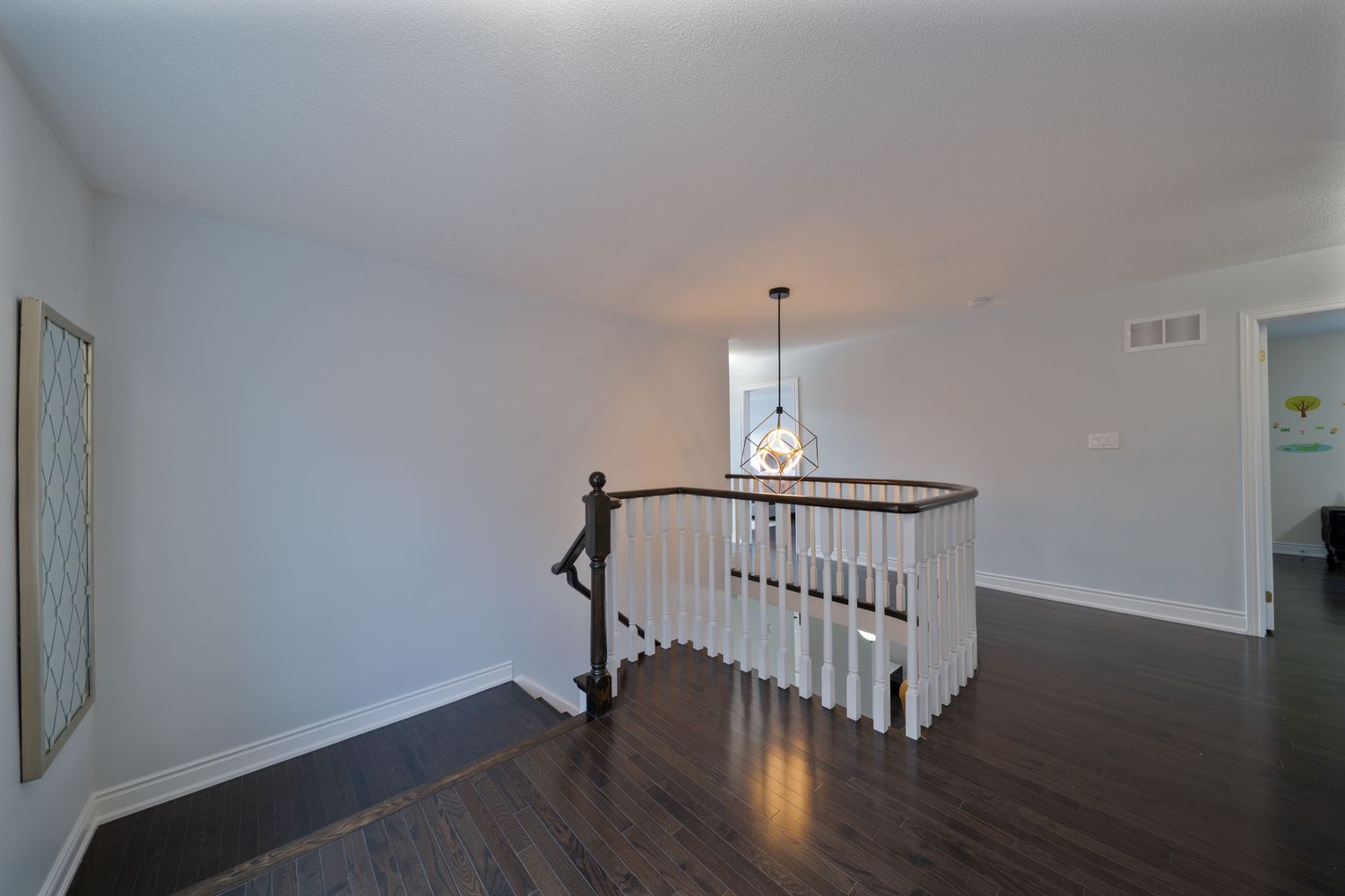 Modern interior hallway with dark hardwood floors and white walls features a sleek staircase with black railings.