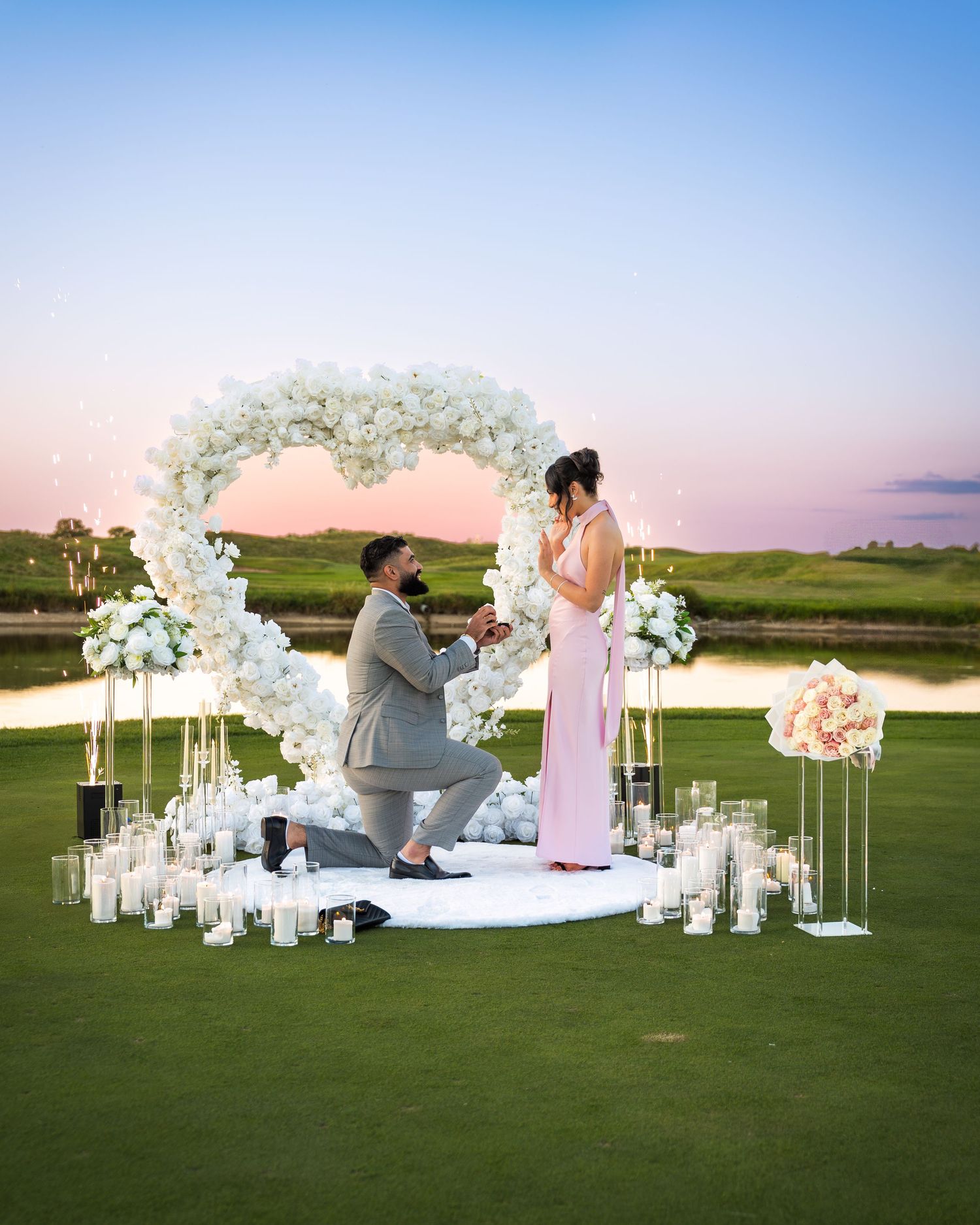 Magical proposal scene with white floral arrangements and lanterns under sunset sky.