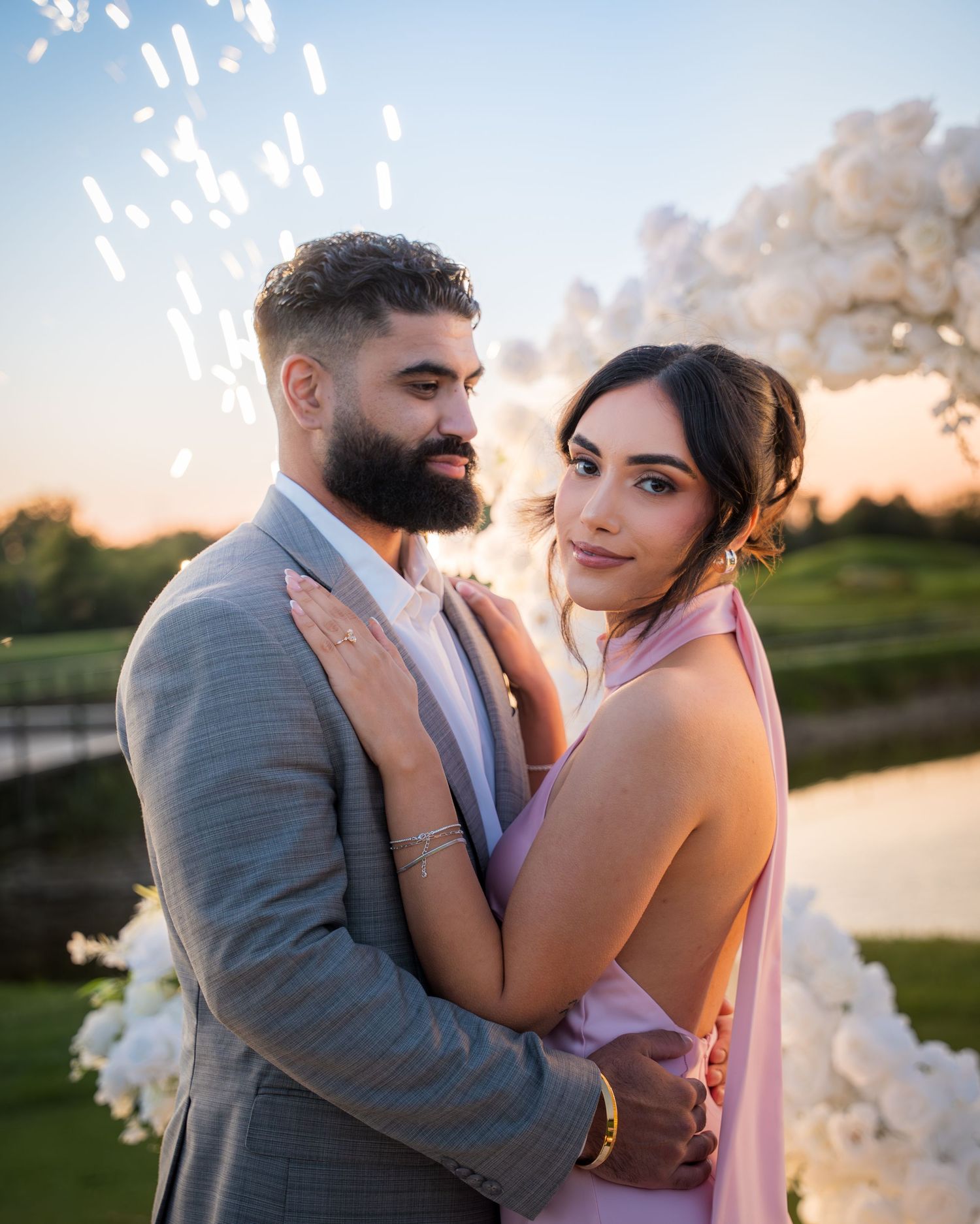 Couple in formal wear shares a tender moment by a lake at sunset.