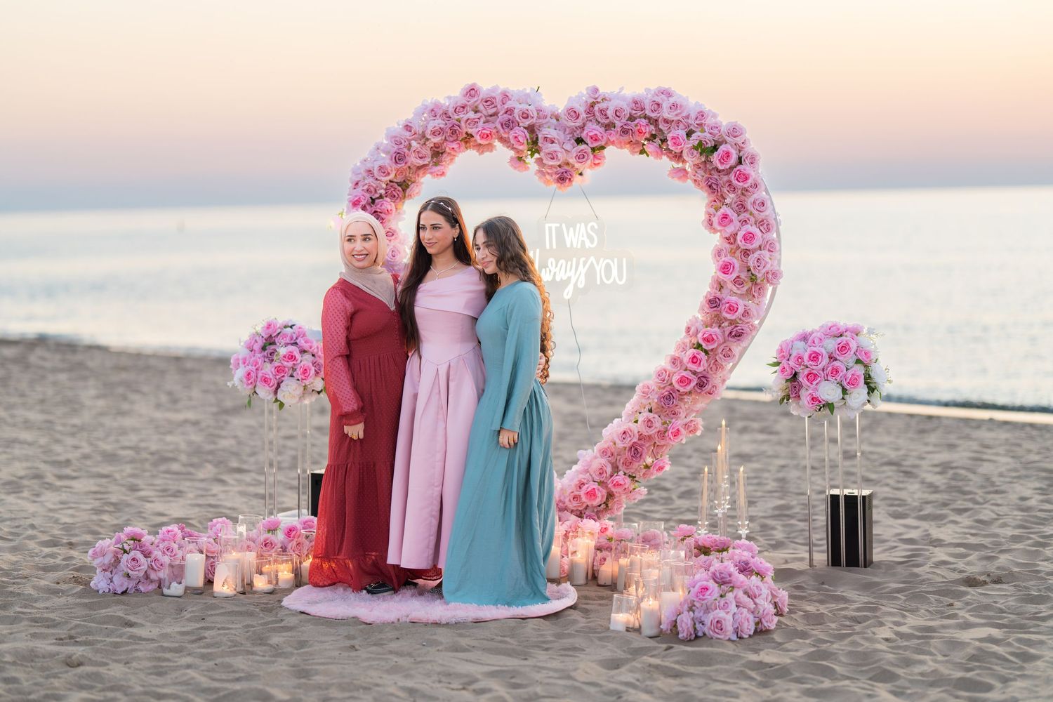 Beach celebration setup with pink heart arch and decorative elements at sunset.