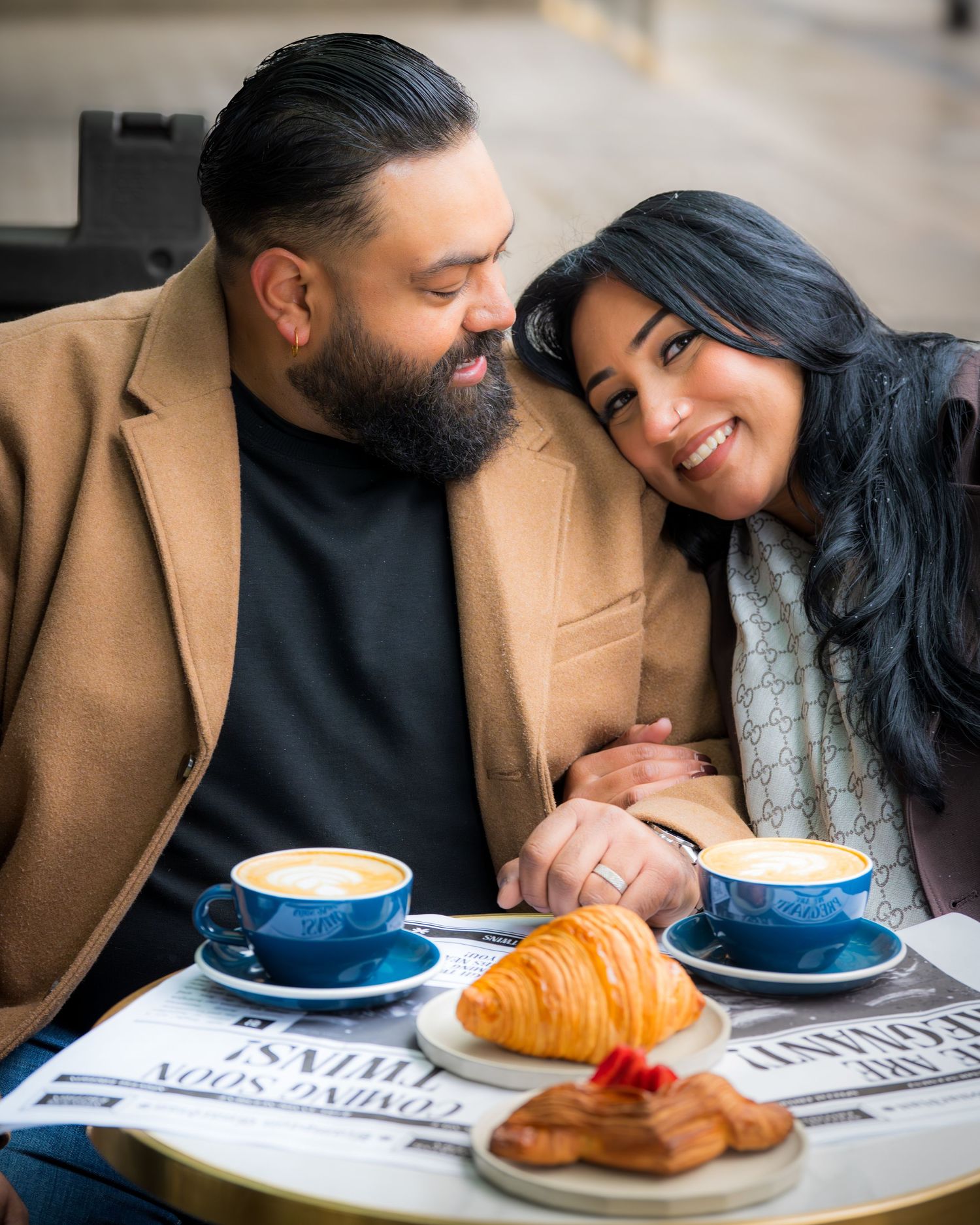 Couple sharing an intimate moment at a cafe with coffee and pastries on a newspaper.