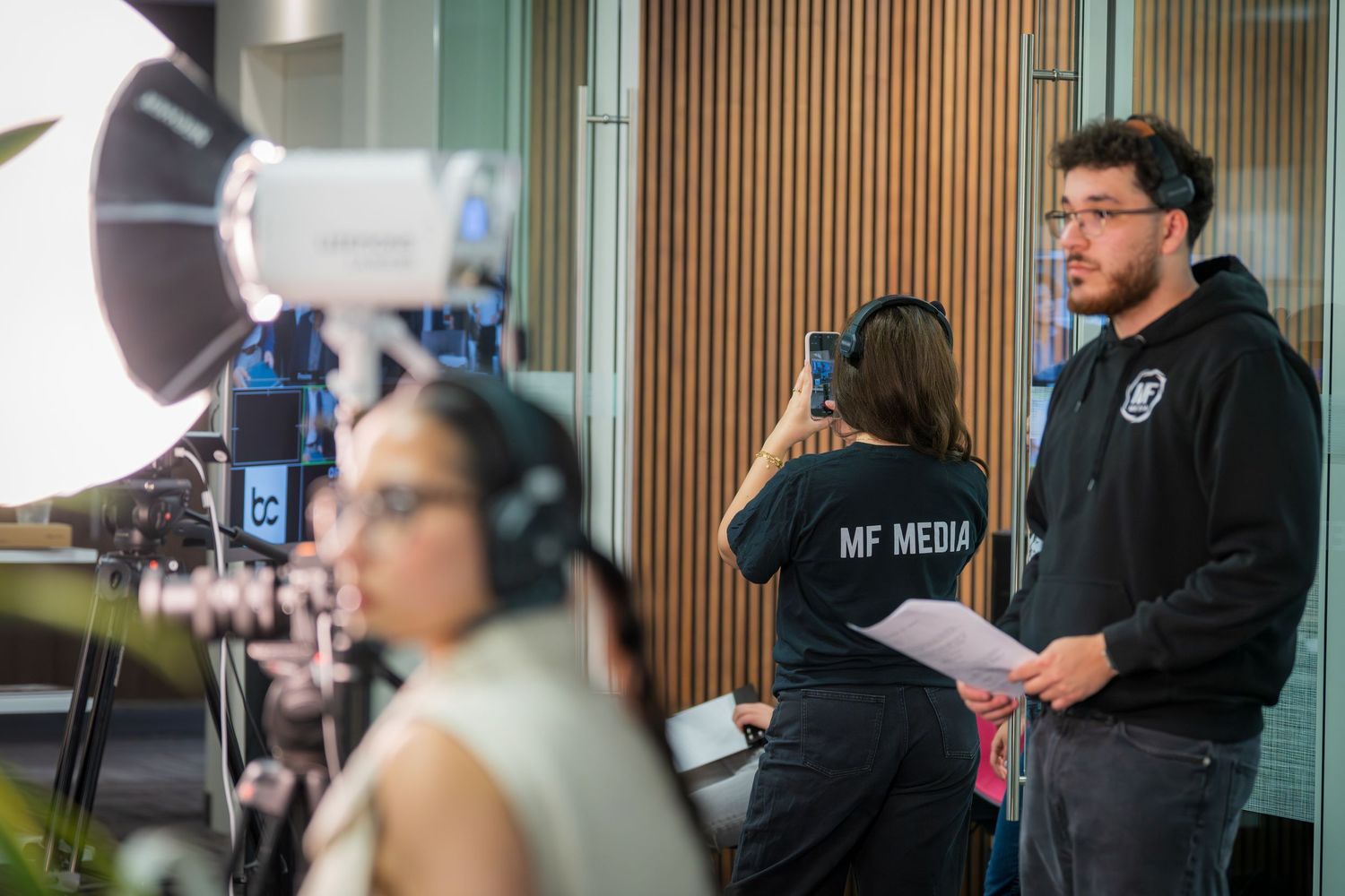 MF Media crew filming on set with professional lighting equipment and camera in modern studio.