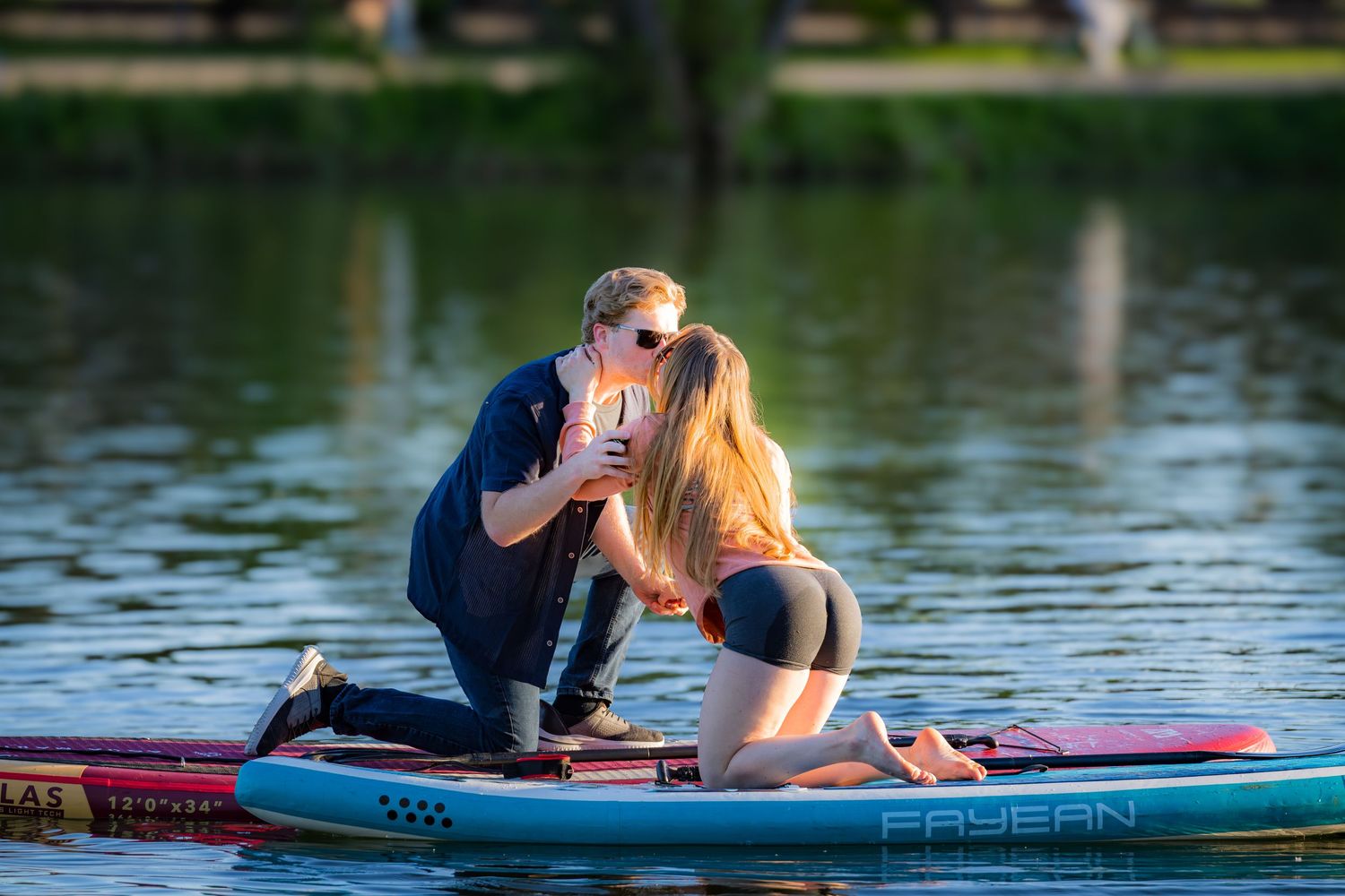 Couple kissing on a paddleboard on a calm lake during a warm sunny day.