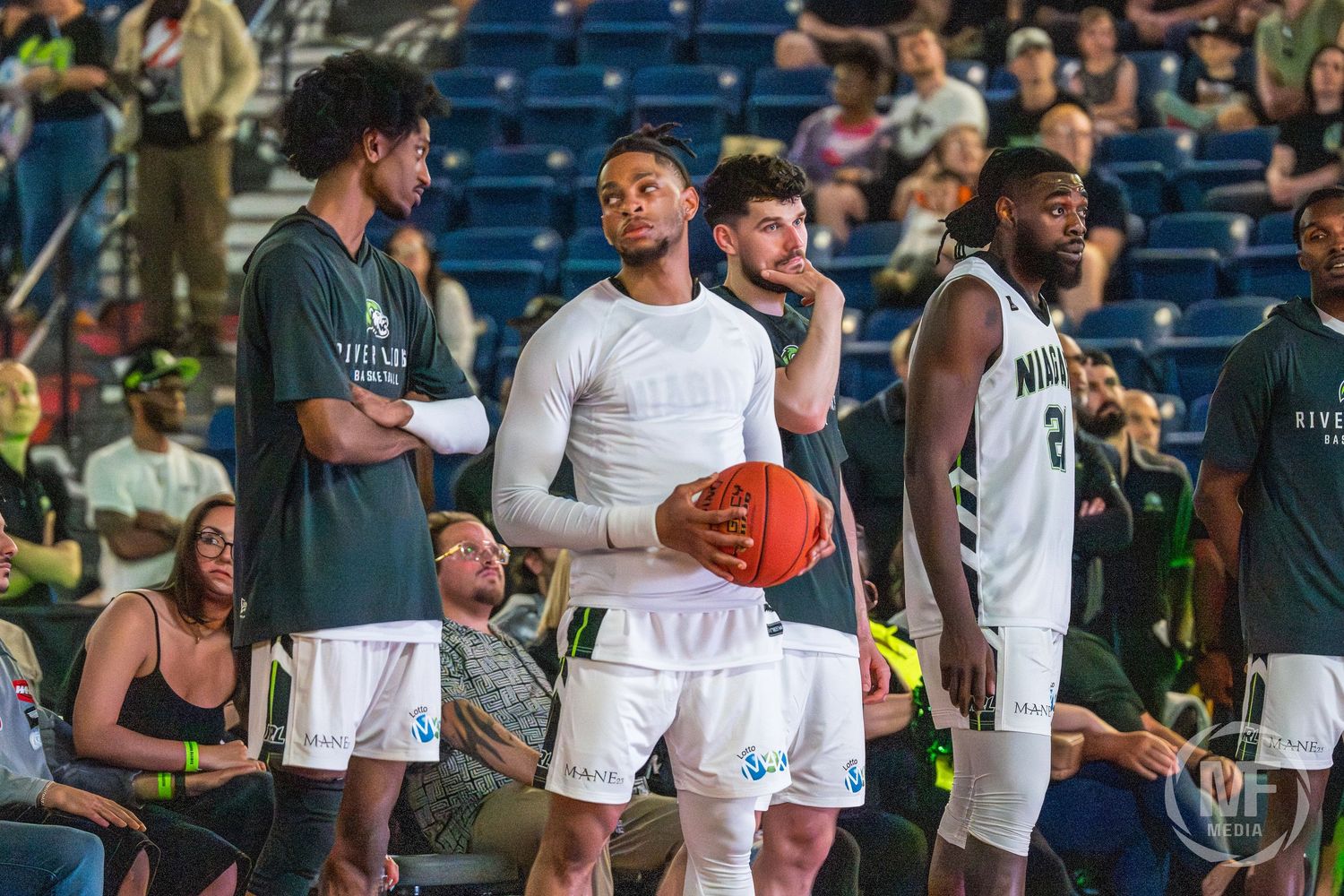 Niagara basketball players in green uniforms stand on the sideline during a game.