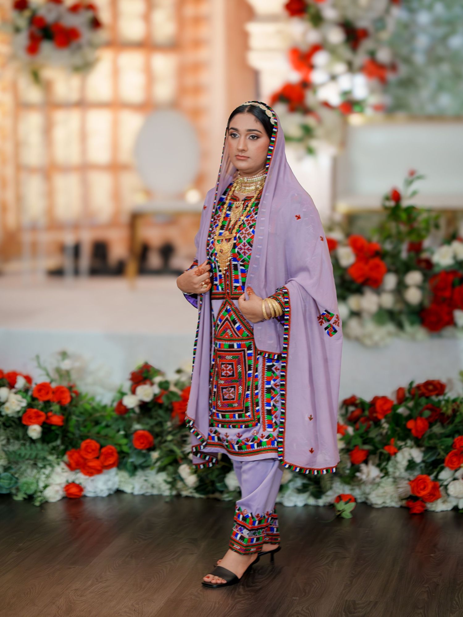Traditional outfit with colorful embroidery against a backdrop of red and white flowers.