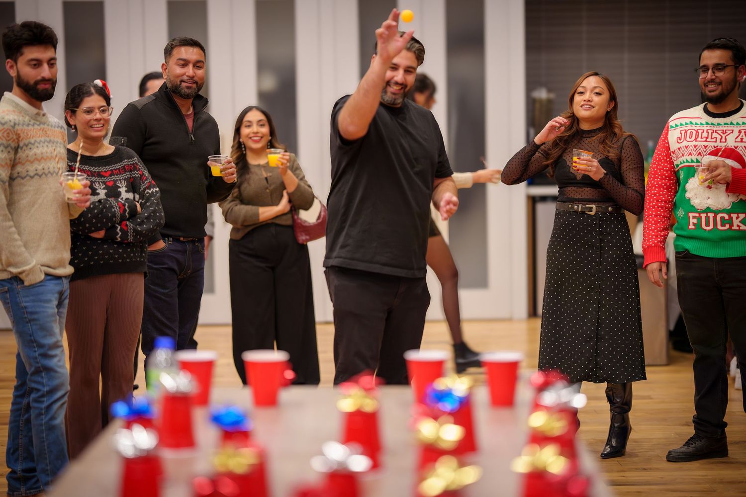 Party attendees gathered around red cups set up on the floor for a game.
