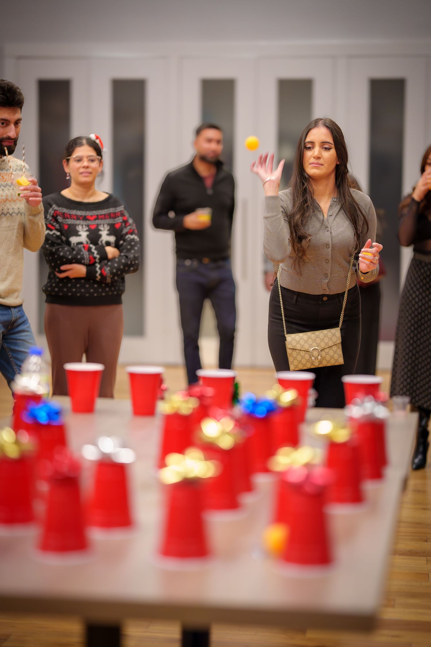 Red plastic cups lined up on a wooden floor for party games with people standing around.