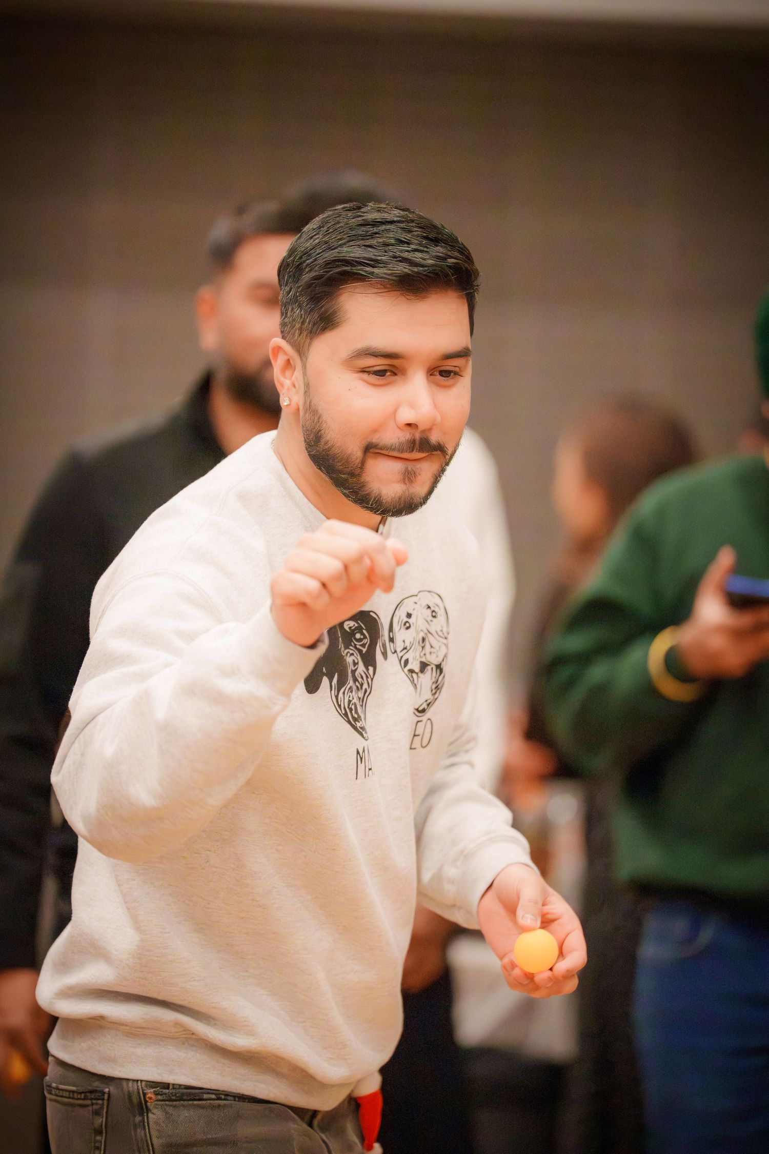 Person in a white sweatshirt smiling and gesturing during an indoor gathering.