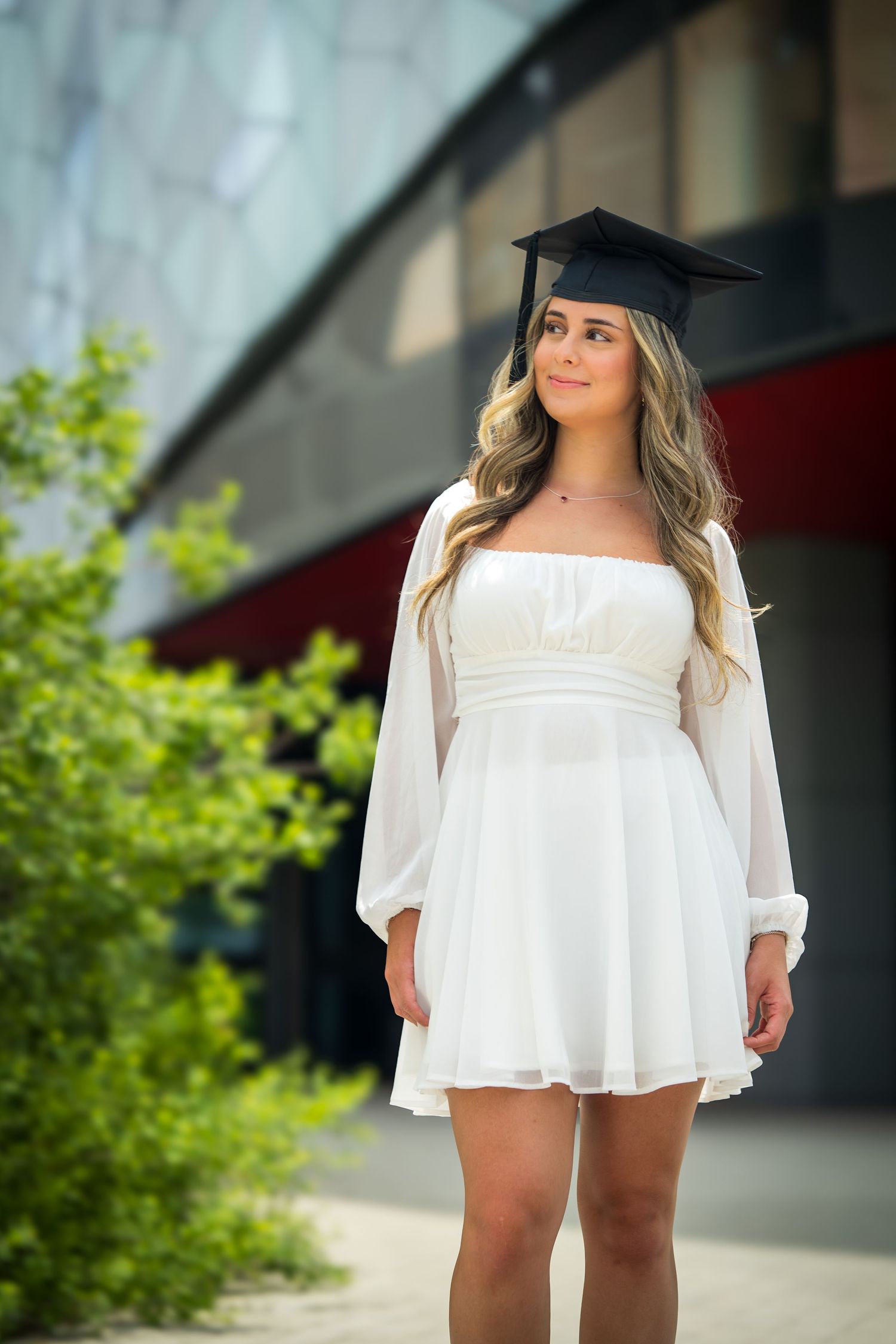 Graduation photo showing white dress and cap against architectural elements.