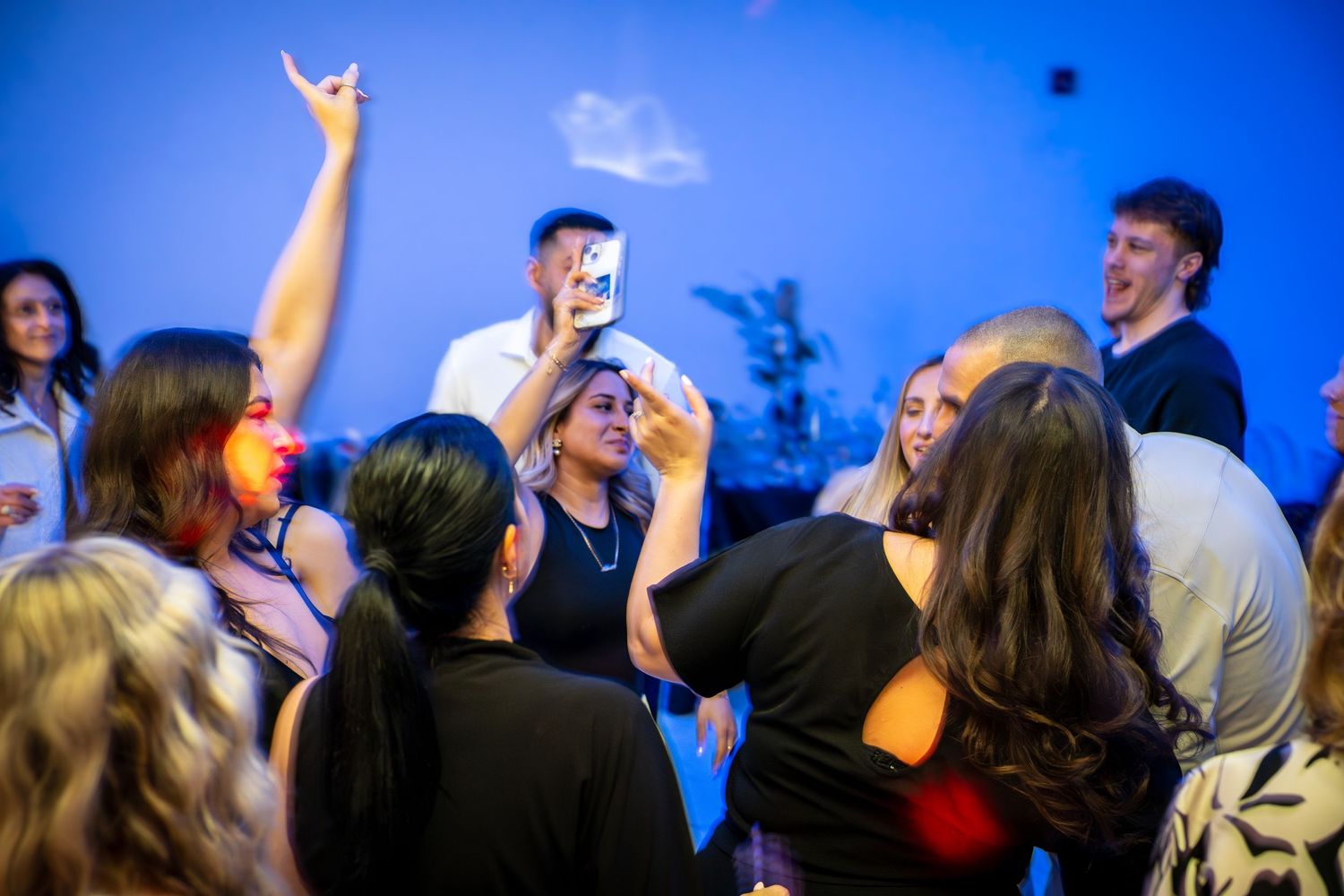 Crowd of partygoers dancing with raised arms under vibrant blue lighting.