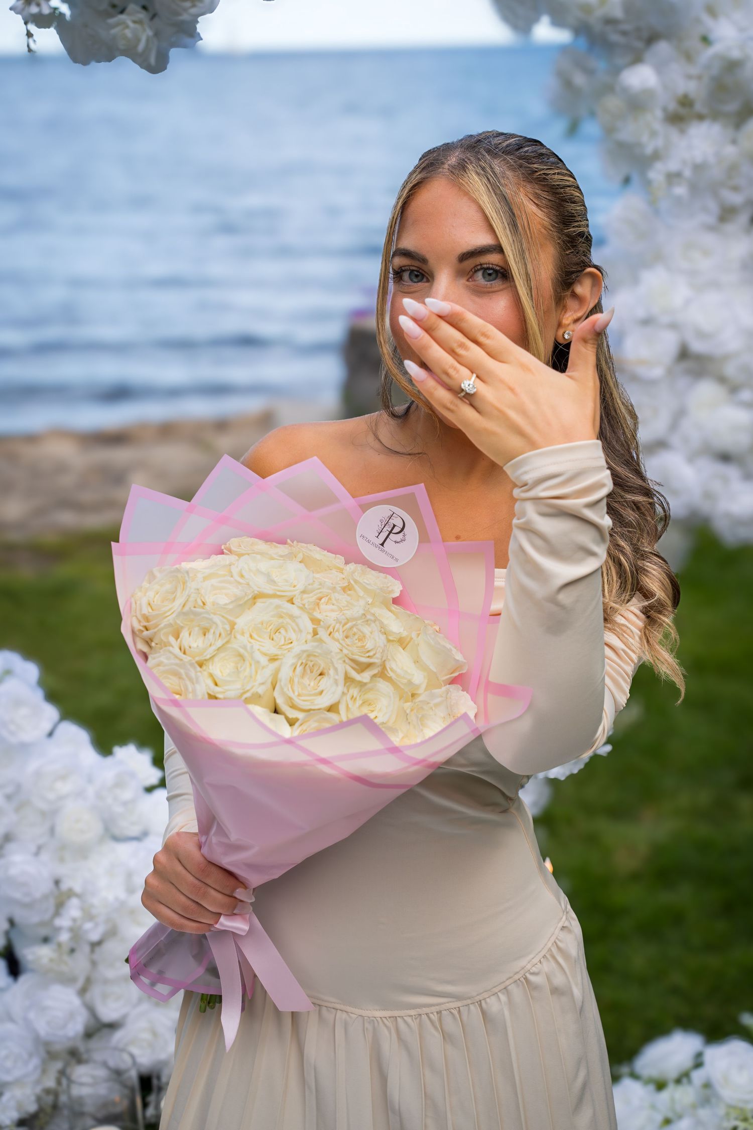 Emotional surprise reaction to a pink and white rose bouquet against a waterfront backdrop.