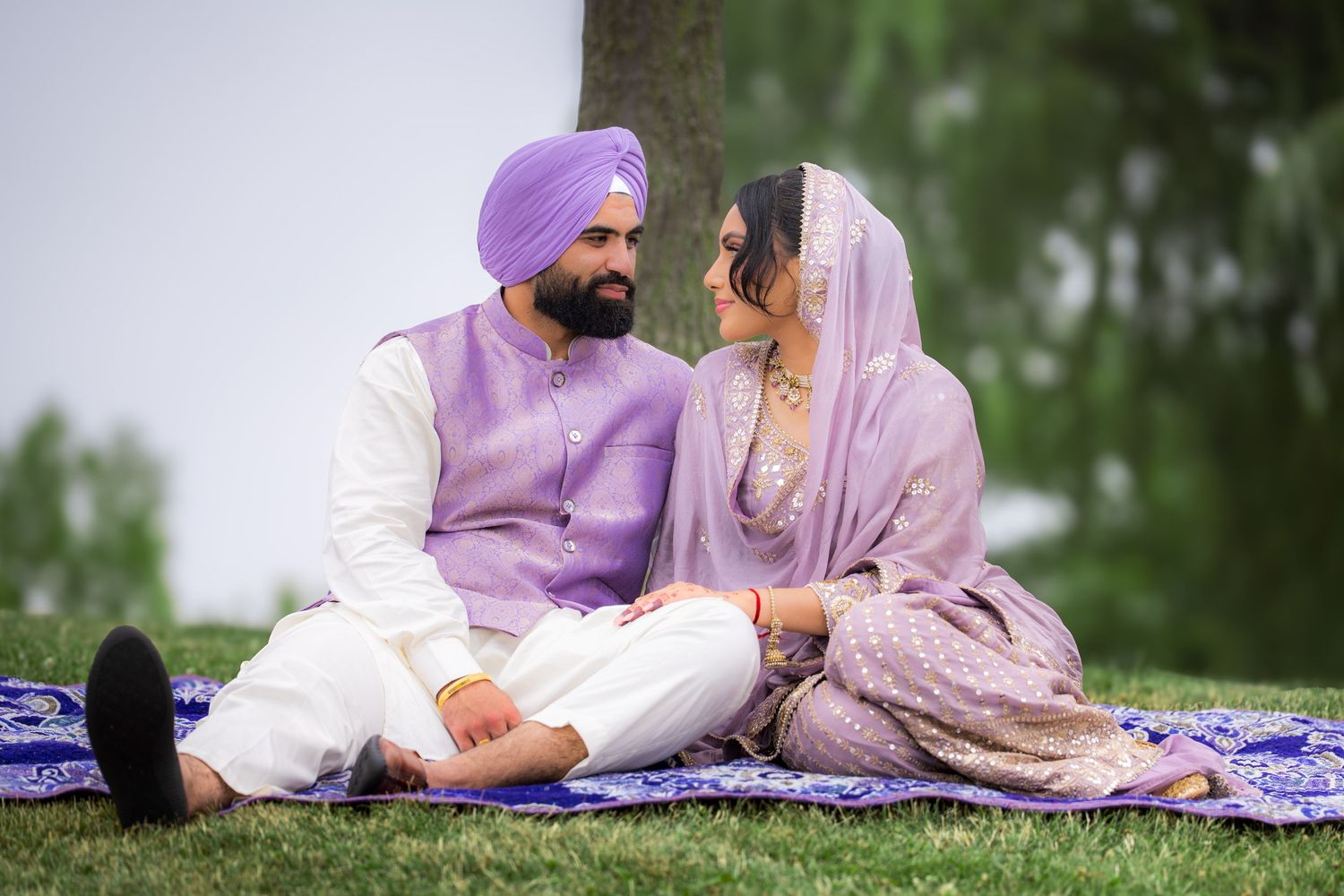 A couple in traditional Indian dress poses together on a blue blanket against a natural backdrop.