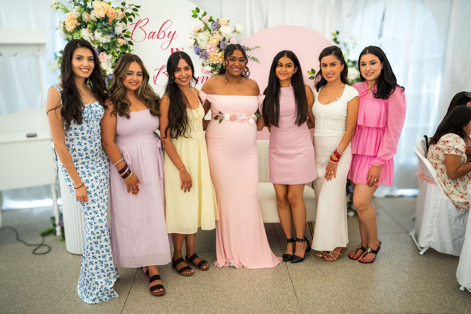 Group photo of attendees wearing coordinated pink and pastel dresses at a baby shower celebration.