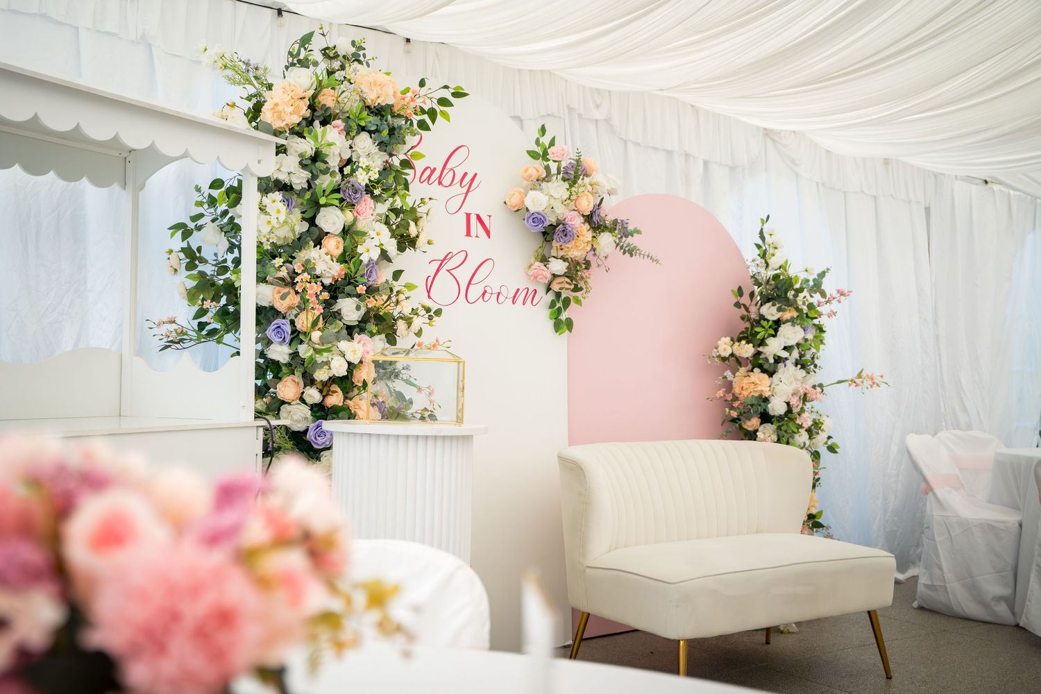 Wedding tent decorated with white draping, pink accents, and floral arrangements.