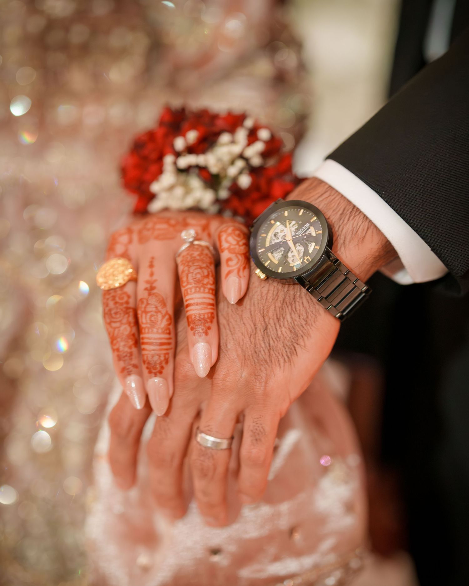 A close-up shot of hands wearing henna designs and jewelry against a soft bokeh background.