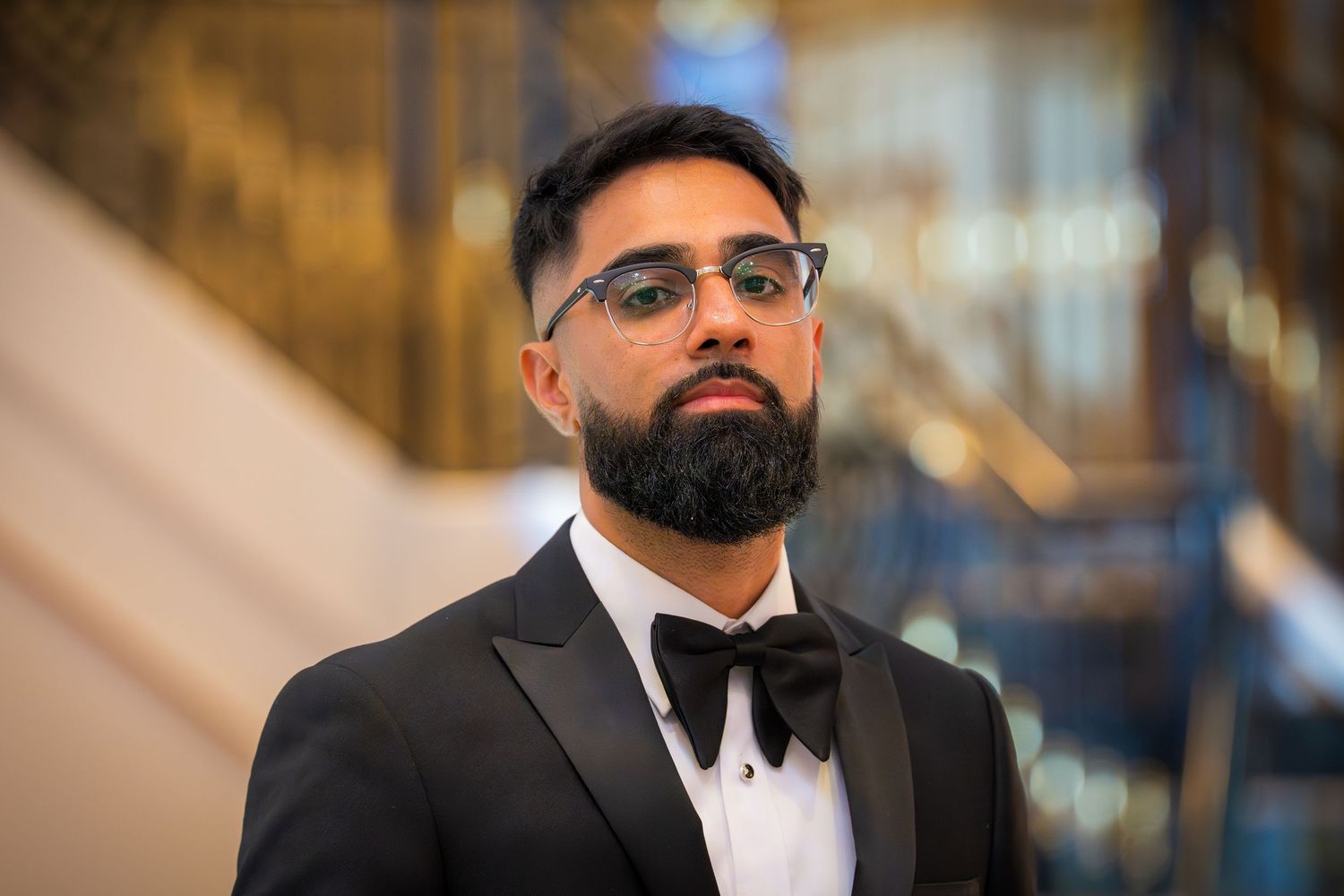 Close-up portrait of groom in classic black tuxedo and glasses at formal event.