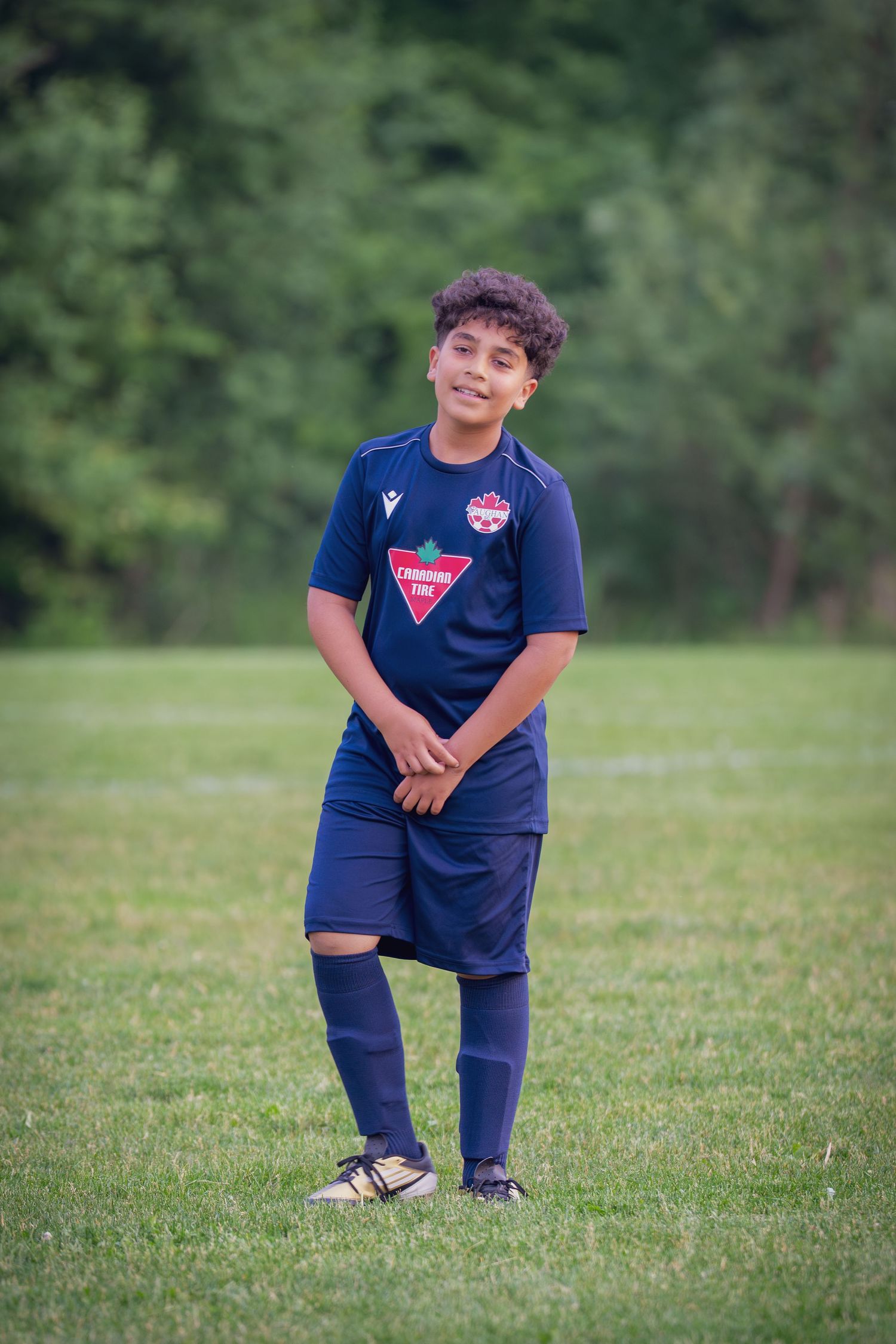 A young soccer player in a navy blue uniform poses on a grassy field during a sunny day.