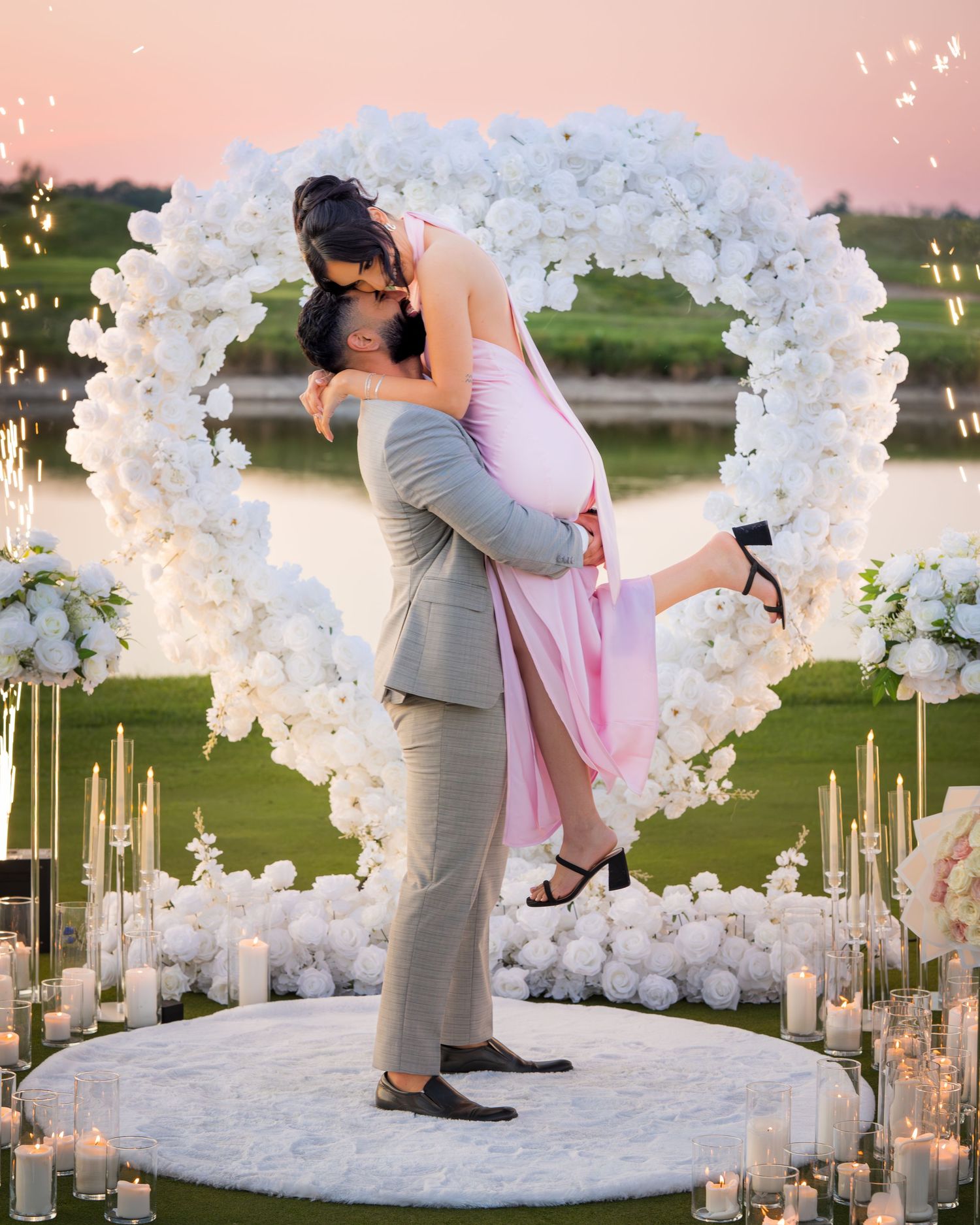Romantic dip pose beneath an ornate white floral arch surrounded by glowing candles.