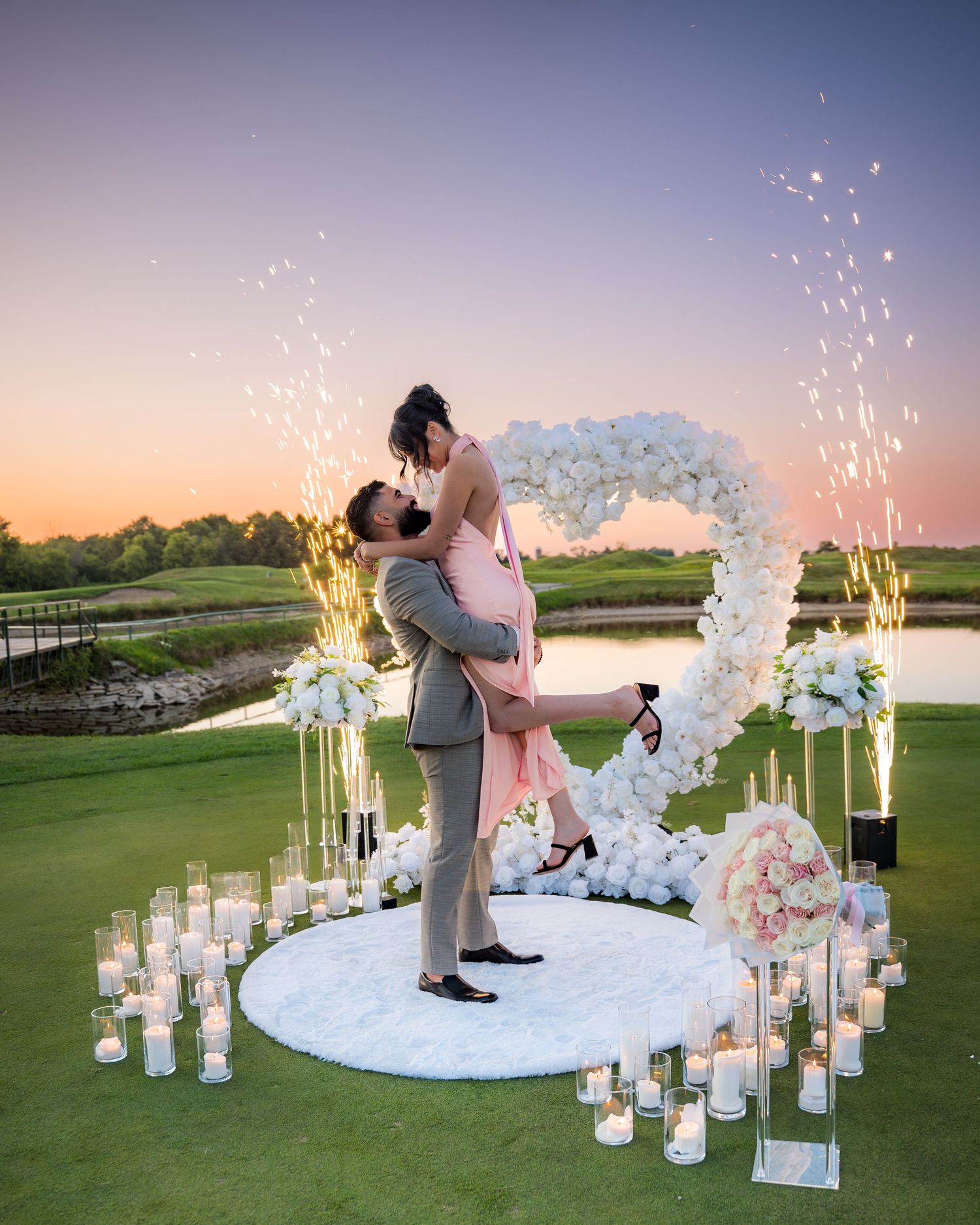 Magical proposal moment on golf course with lit candles and white floral arrangements.