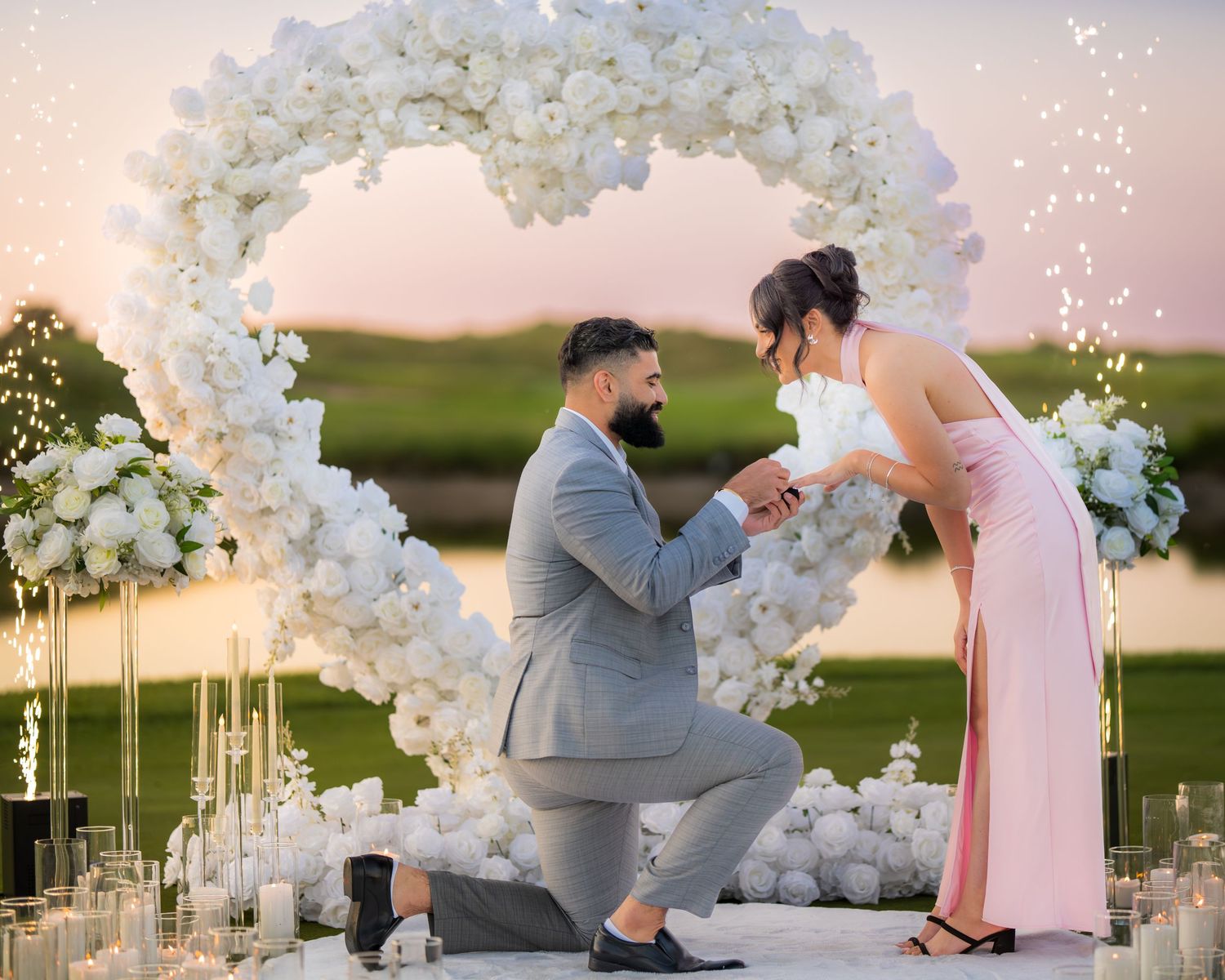 Elegant lakeside proposal with white floral arch and romantic candle arrangements.
