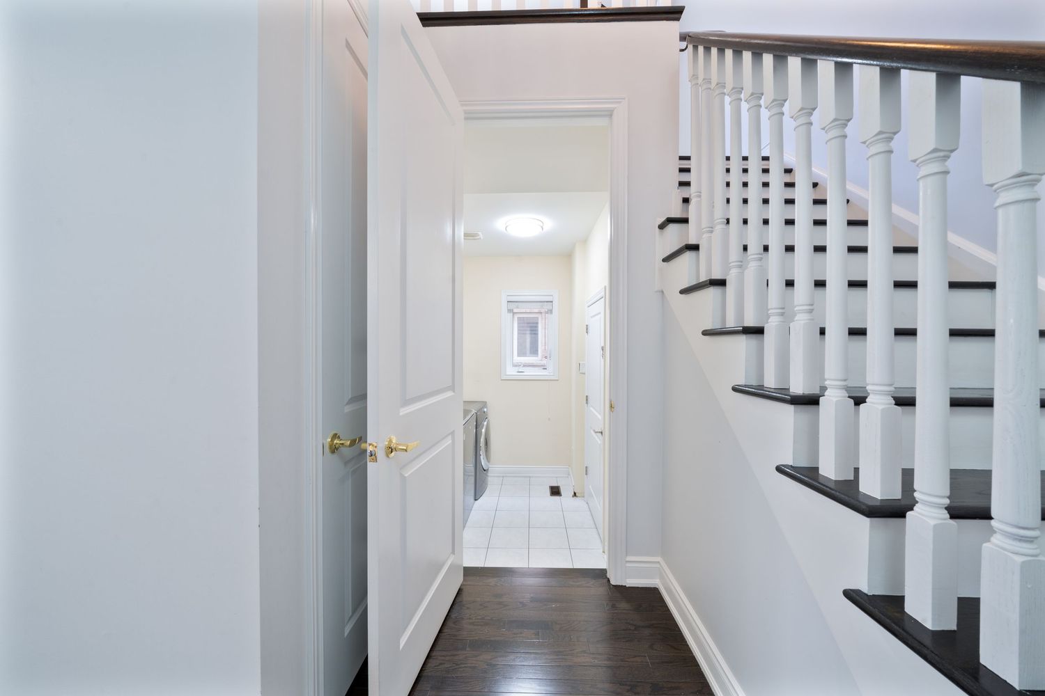White painted hallway with hardwood floors and traditional staircase featuring dark wood handrails and white balusters.