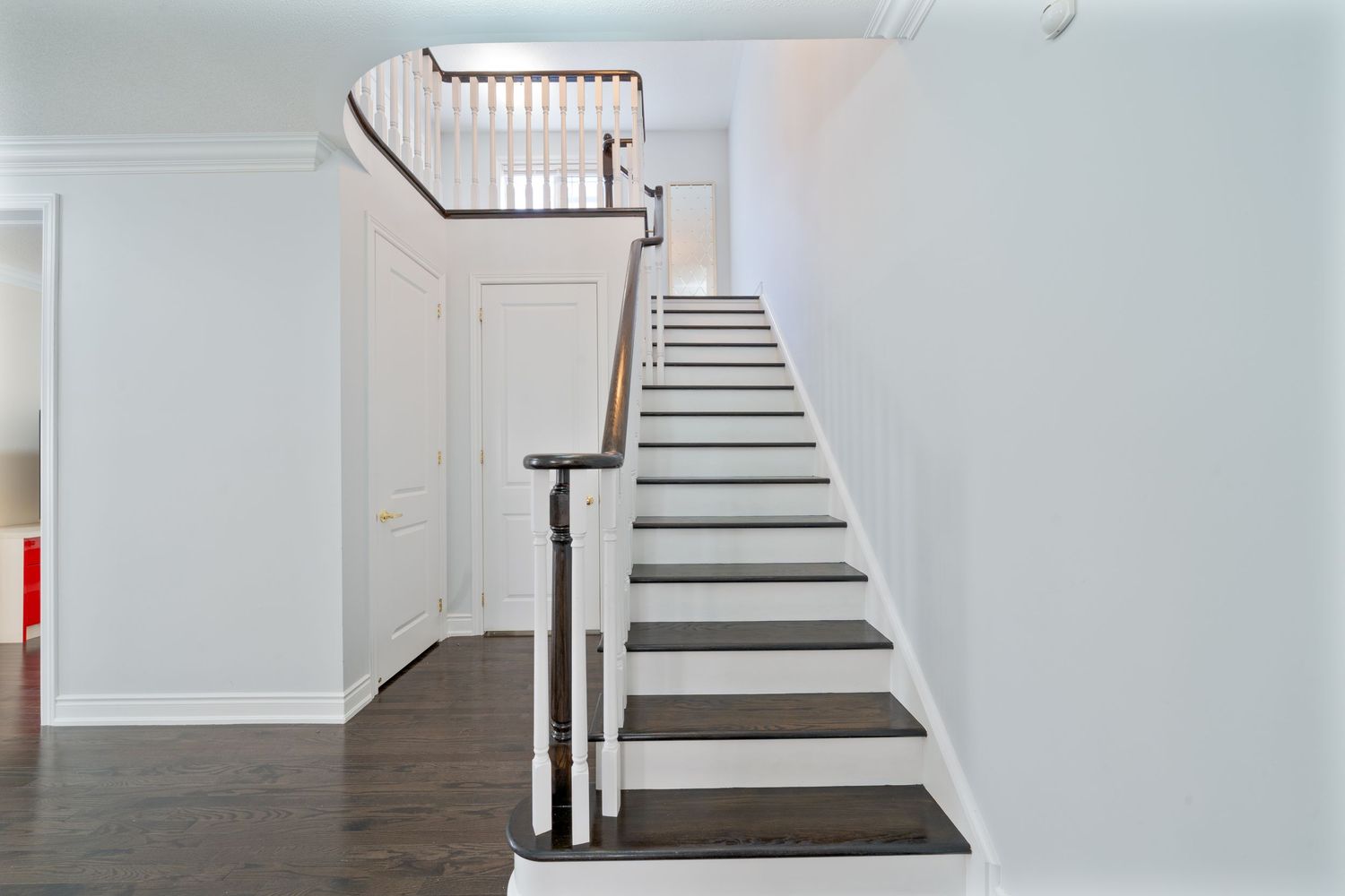 Modern white staircase with dark wood treads and sleek handrail in a minimalist interior space.