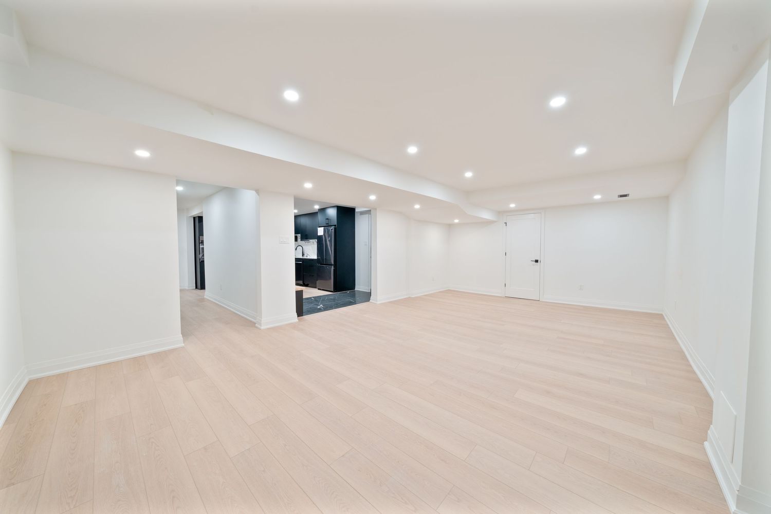 Modern open concept office interior with light wood floors, white walls, and recessed lighting in a minimalist design style.