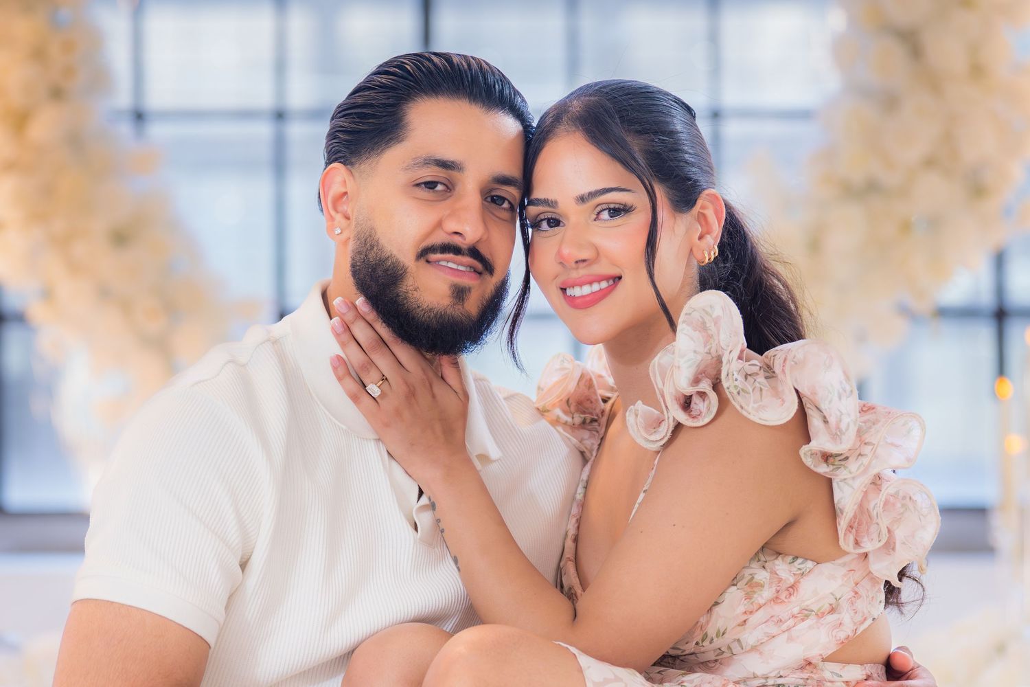 Smiling engaged couple posing together in front of sparkling floral backdrop for engagement photos.