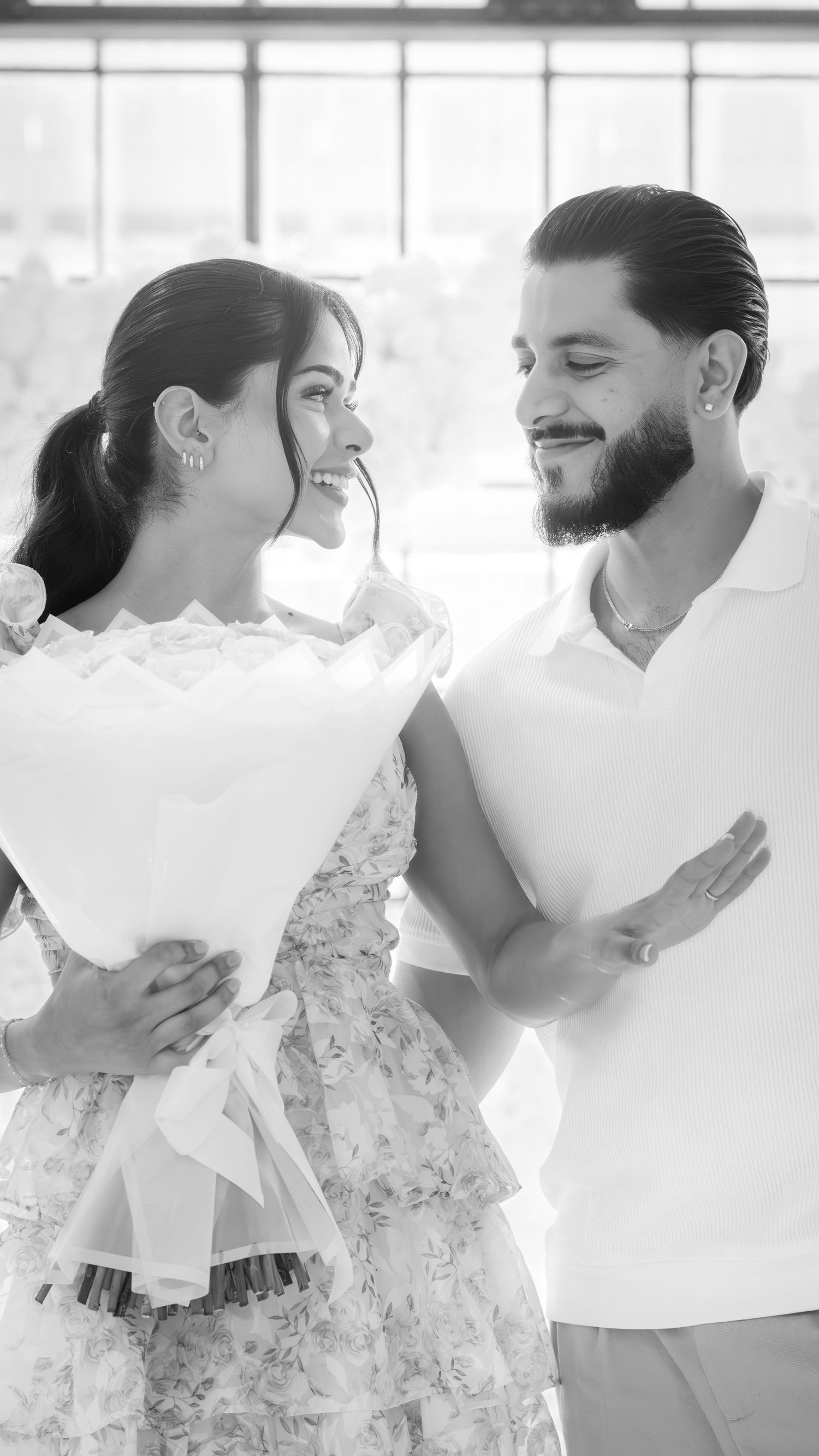 Black and white photo of smiling couple holding flower bouquet during engagement celebration.