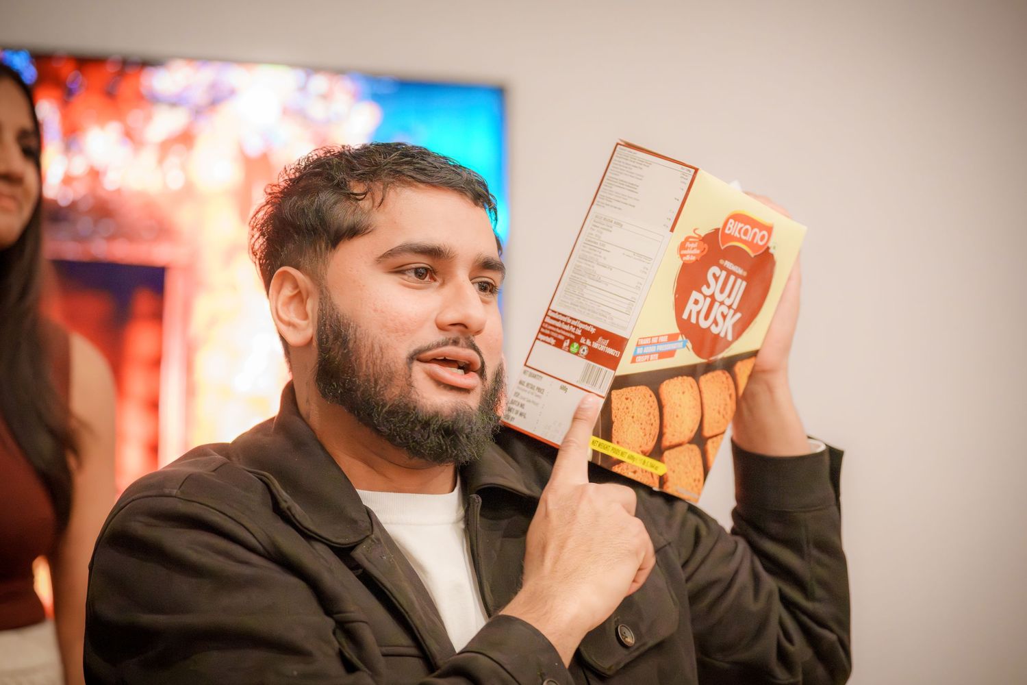 Person gesturing while speaking at an indoor event with screens visible.