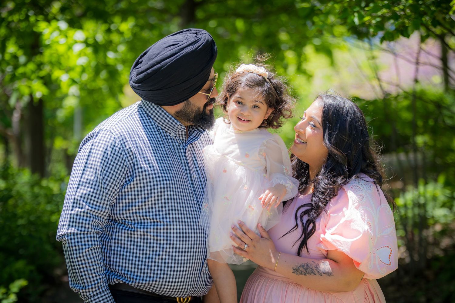 Happy Sikh family with father in turban, mother in pink dress, and young daughter in park.