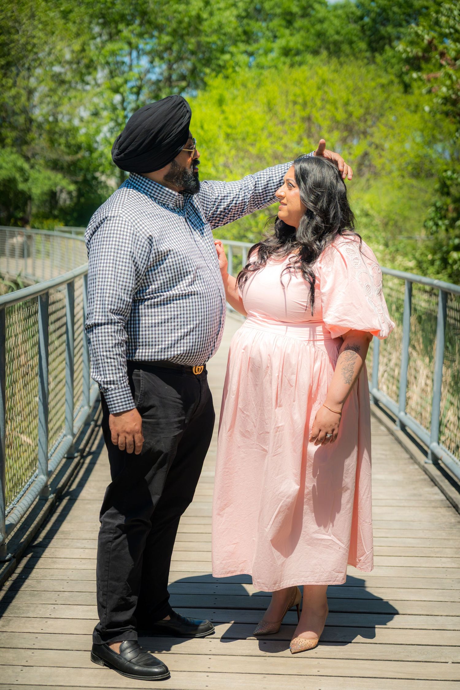 A Sikh man in a turban gently touches a woman's hair as they share a romantic moment on a wooden bridge.