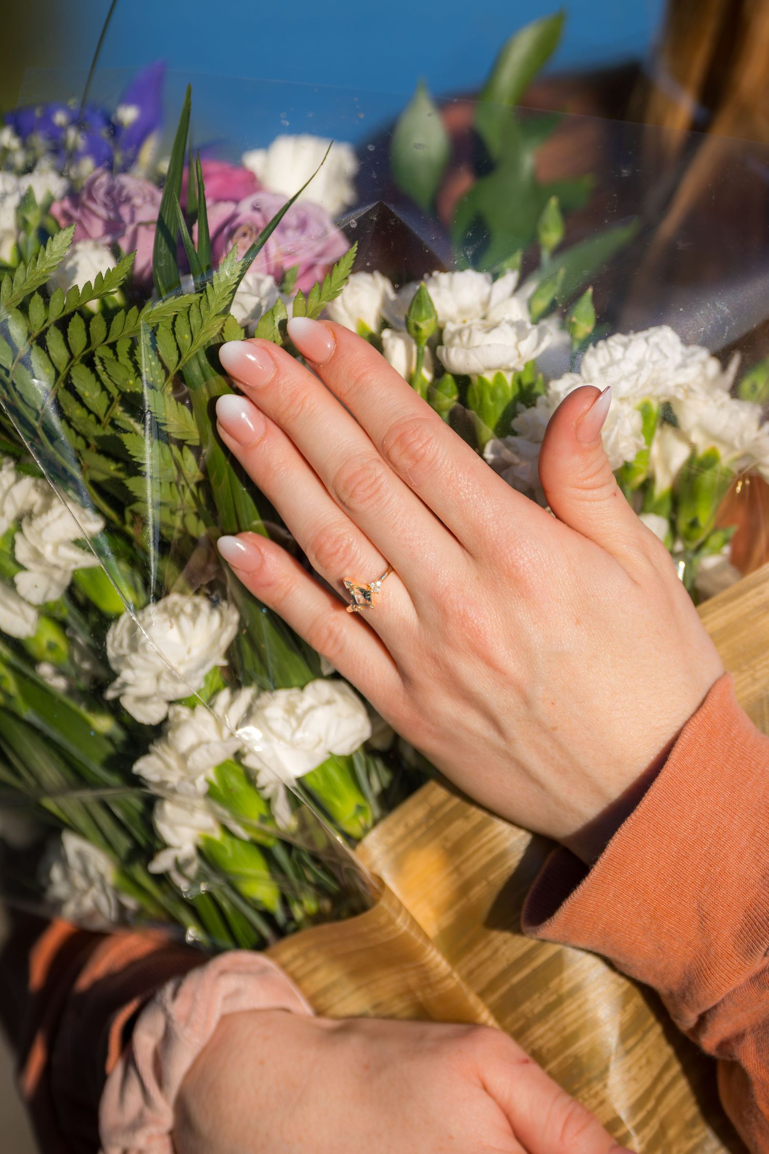 Close-up of a womans hand displaying an engagement ring resting on a bouquet of white flowers.