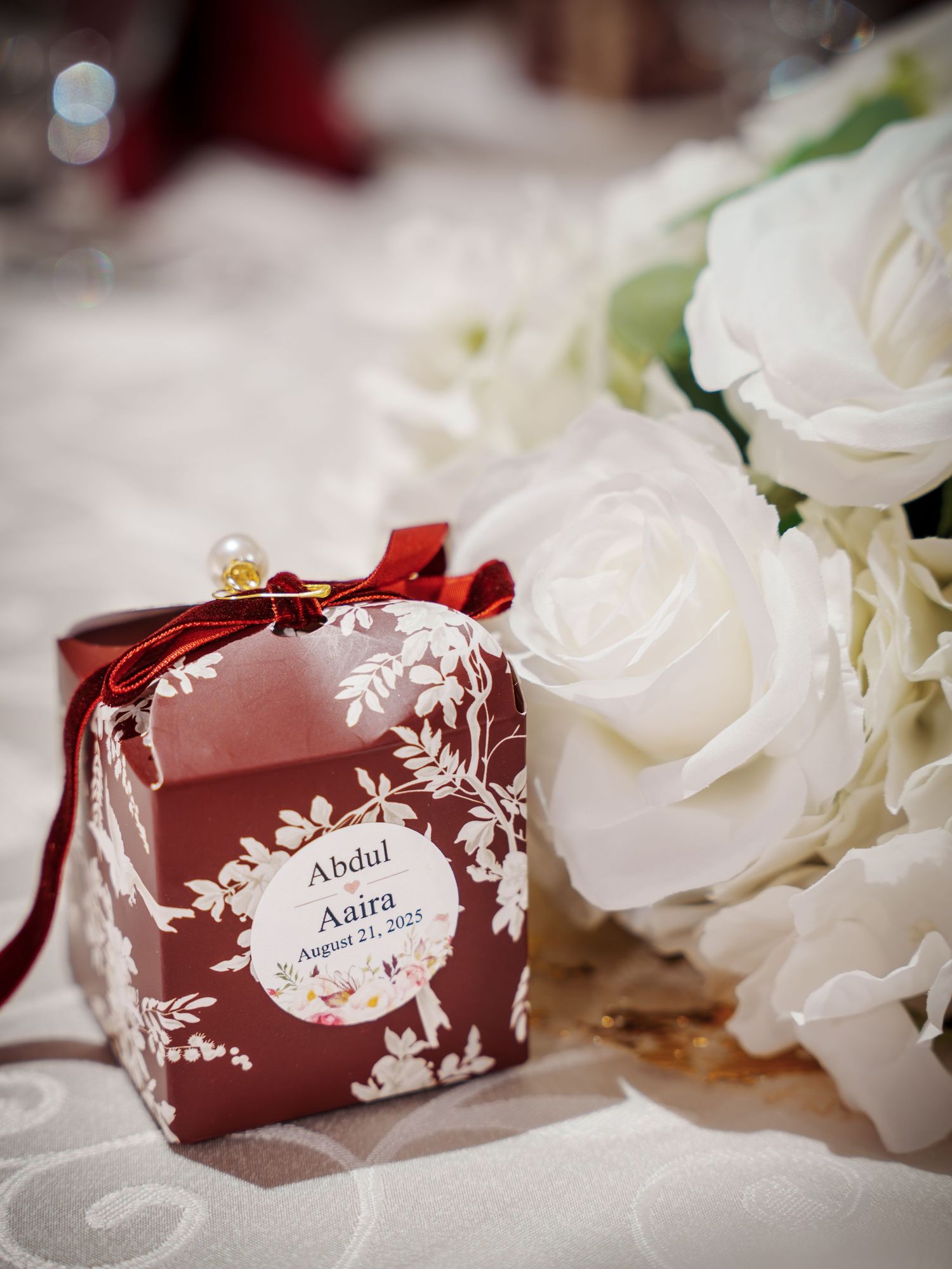 Burgundy wedding place cards with white floral design displayed next to white roses.