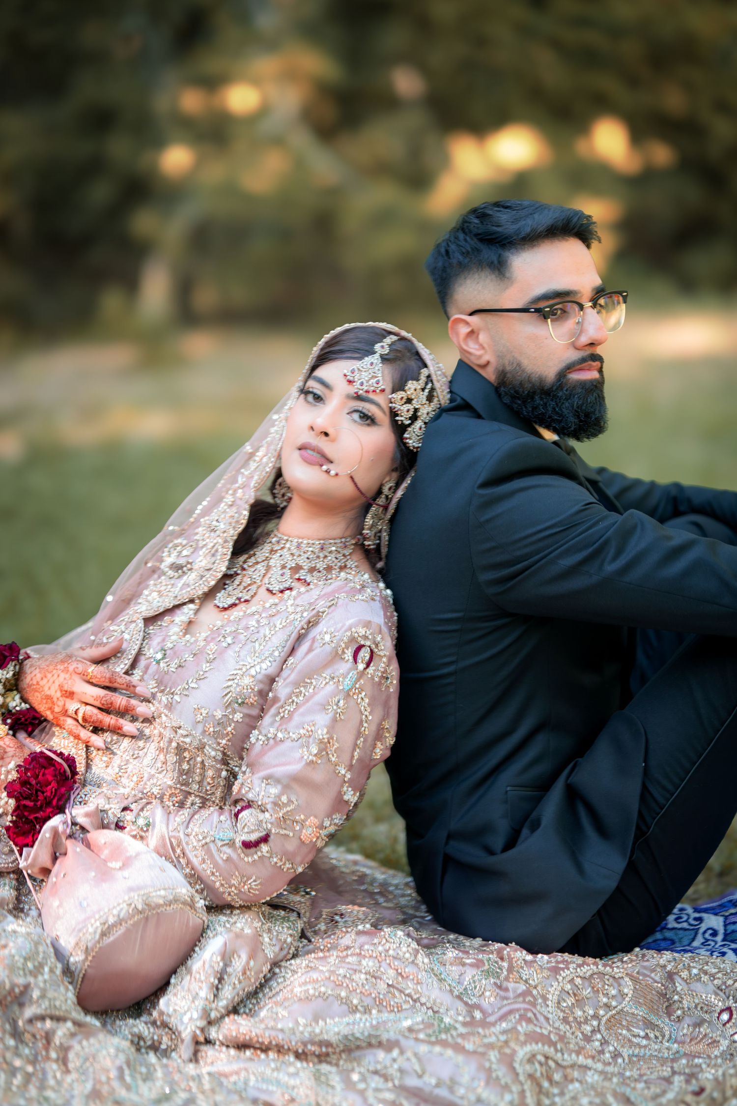 Couple in traditional South Asian wedding attire pose romantically outdoors with bride in shimmering pink lehenga.
