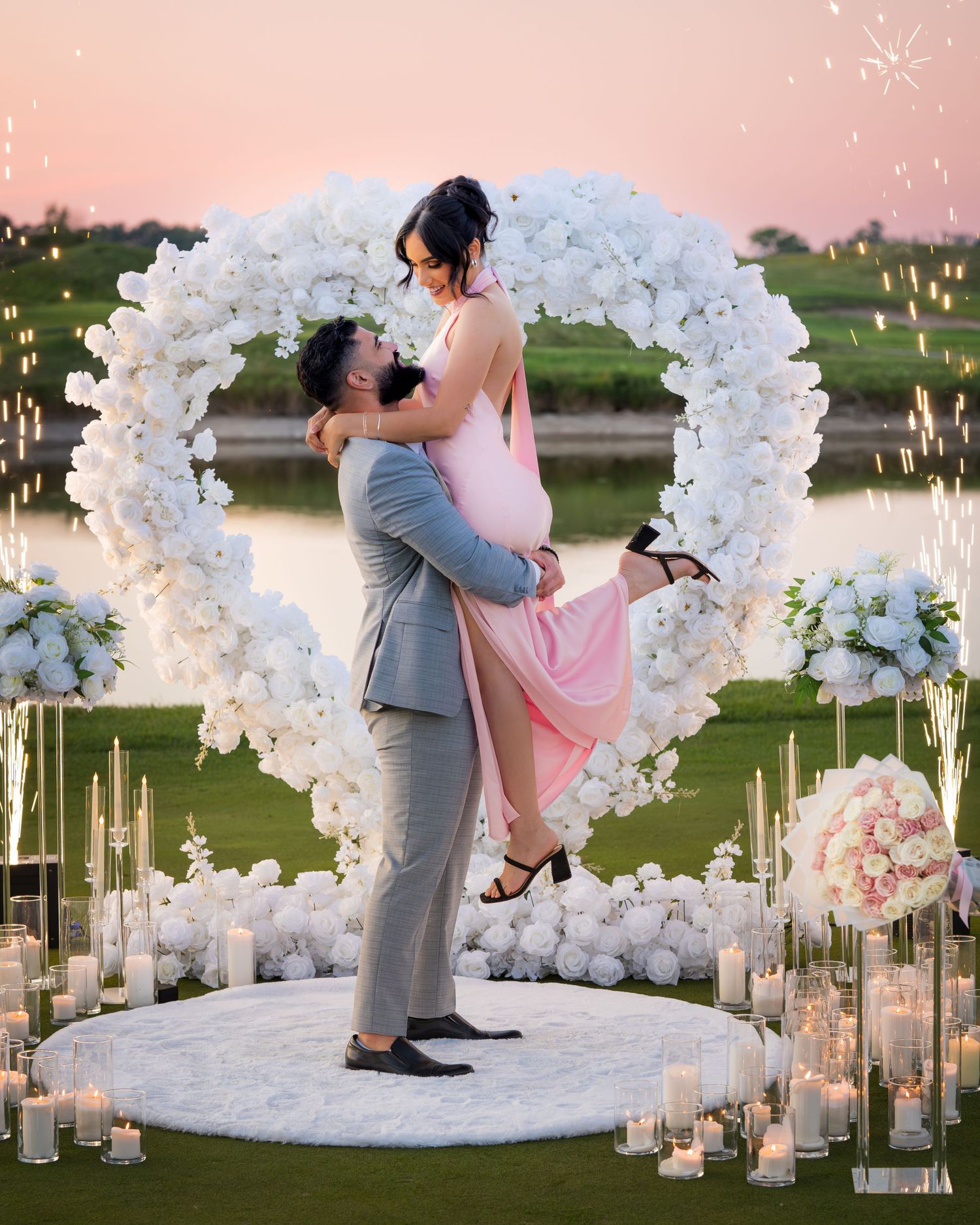 Elegant outdoor wedding moment under a white floral arch with candlelit walkway.