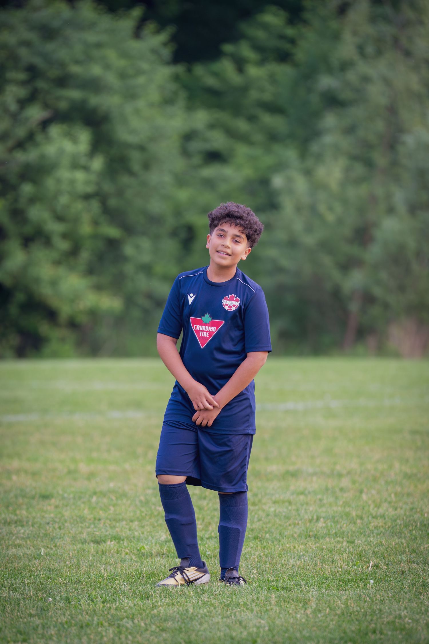 Young soccer player in navy blue uniform poses playfully on a grassy field during practice.