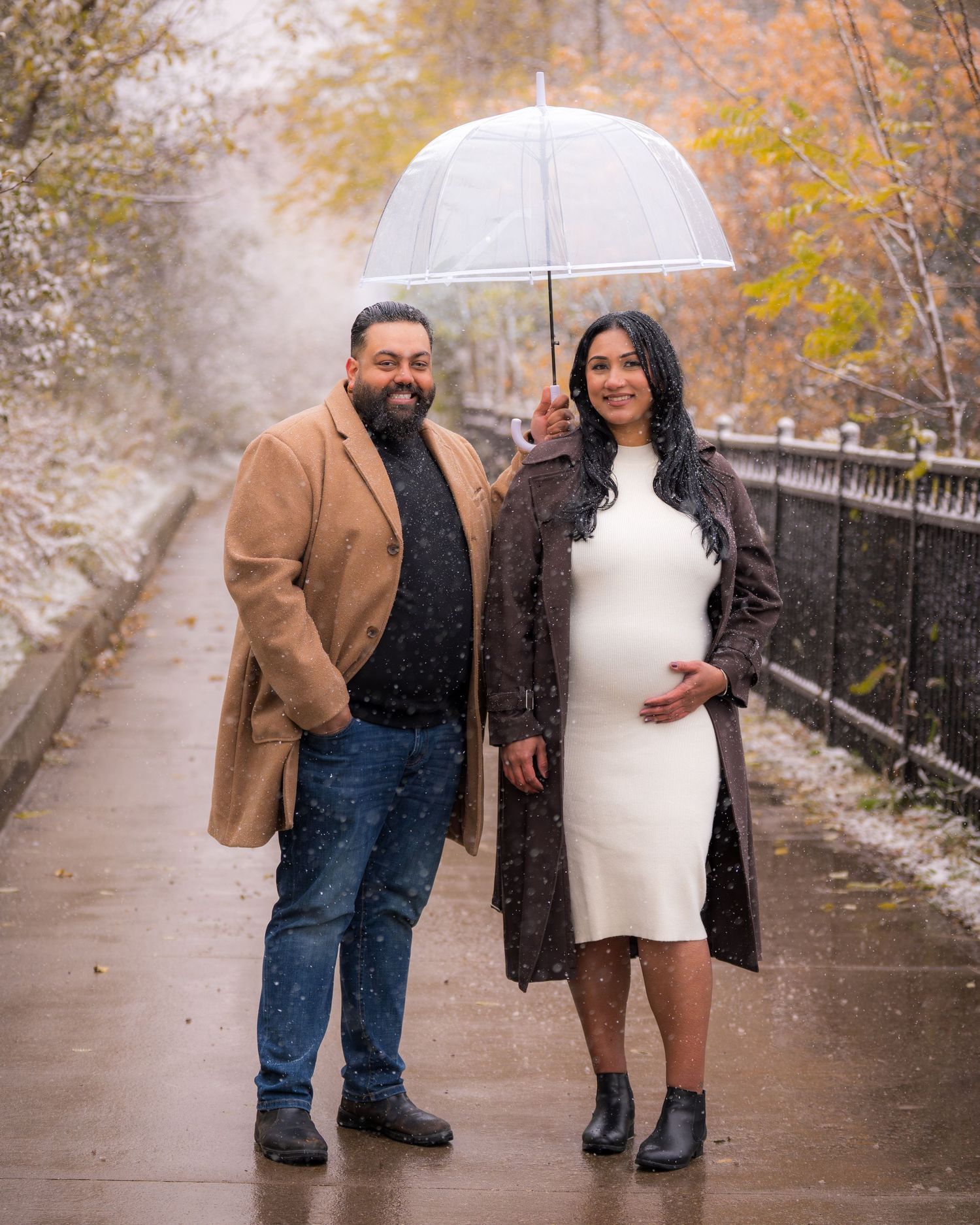 Couple sharing intimate moment on bridge during snowy autumn photoshoot.