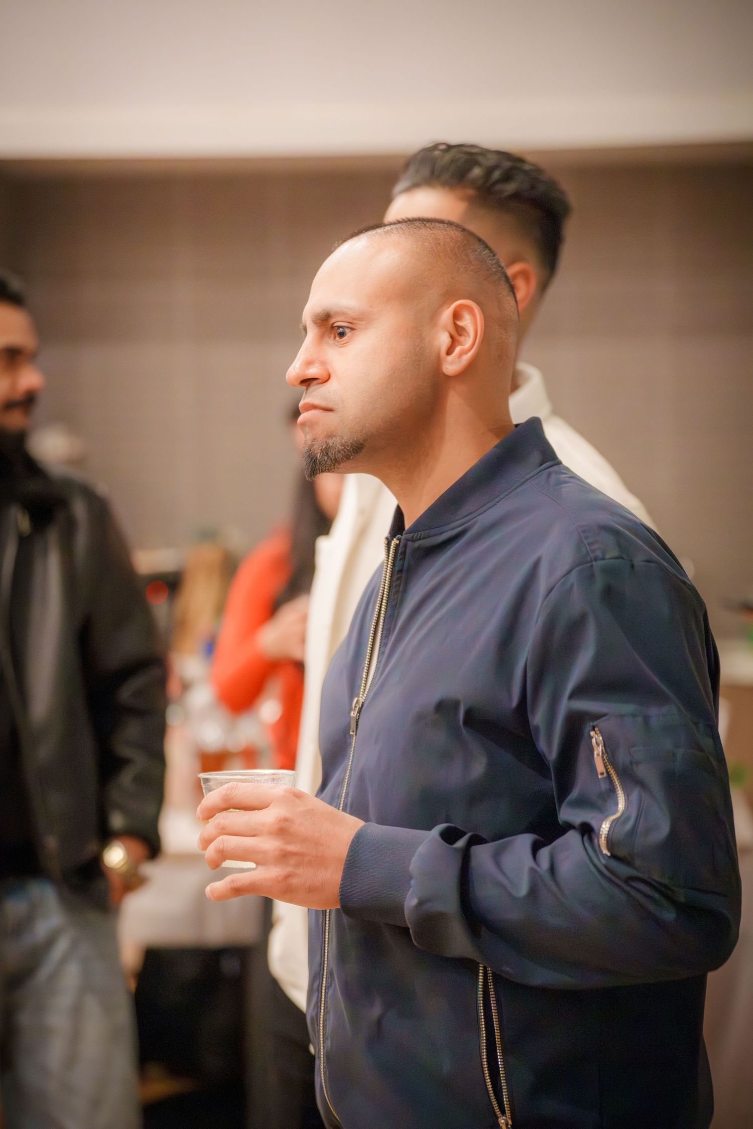 A person in a navy blue jacket gestures animatedly while speaking in an indoor setting.